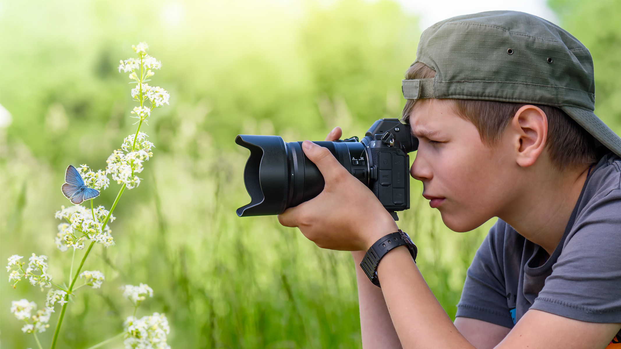 garçon photographier une fleur et un papillon dans un champ