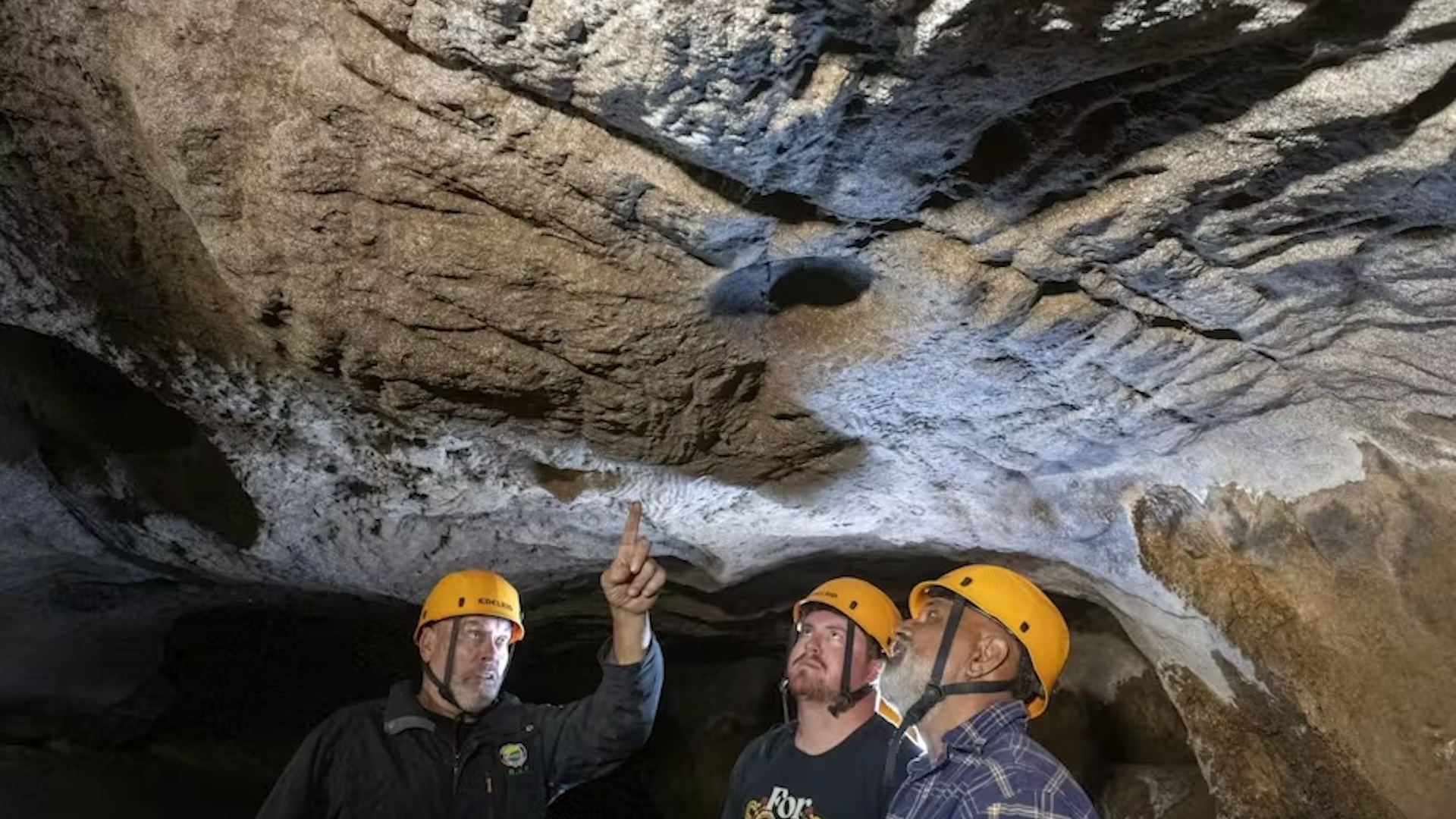 trois chercheurs montrent des rainures de doigts sur le plafond de la grotte