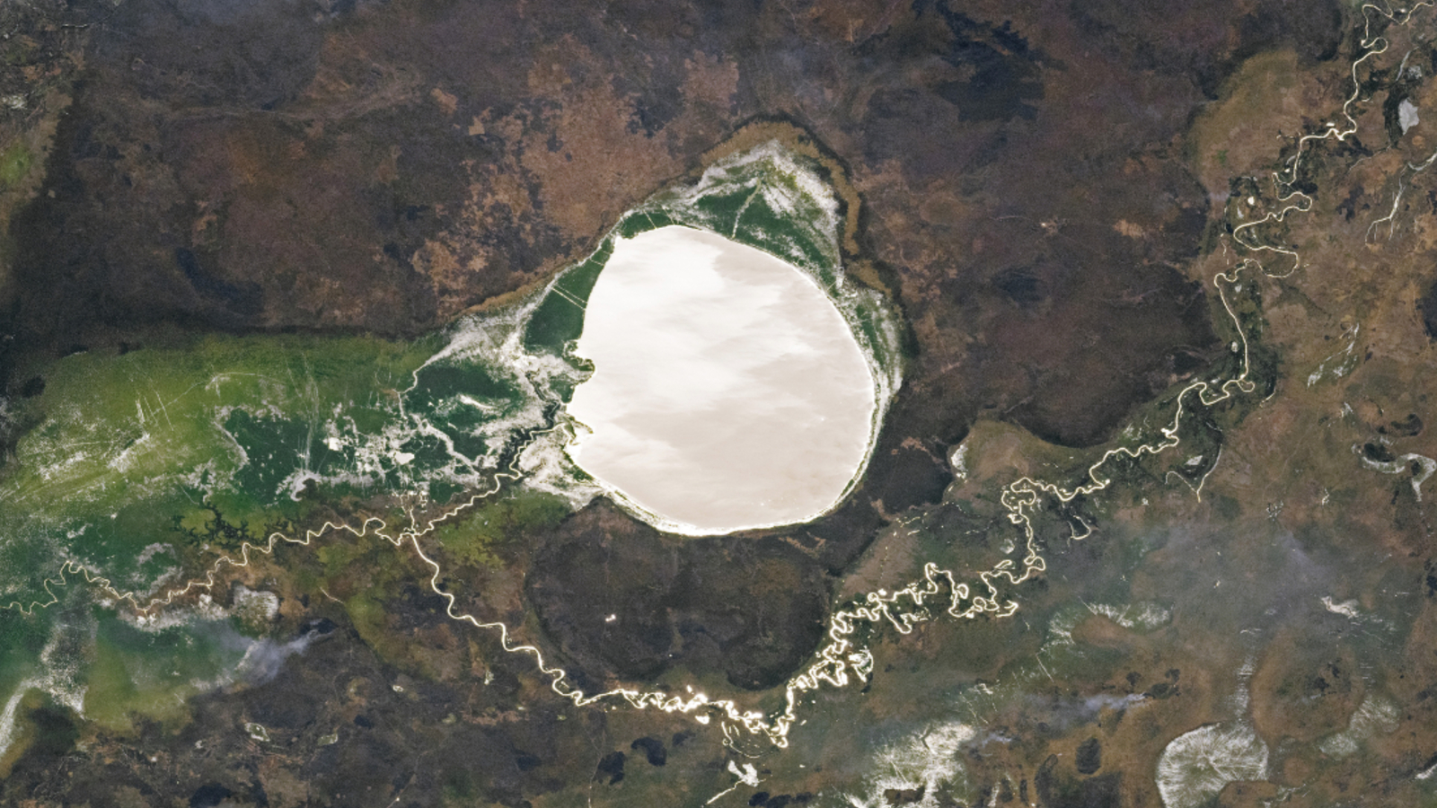 Une photo satellite d'un grand lac arrondi brillant comme un miroir le long d'une rivière venteuse