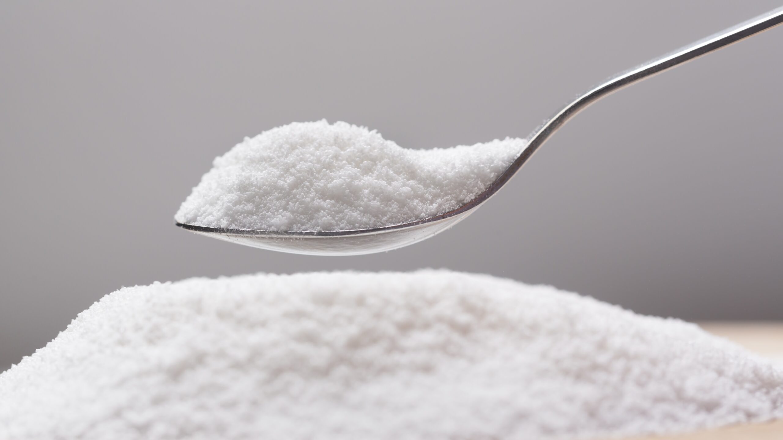 pile of flaky white sweetener on a spoon, above a larger pile of the sweetener