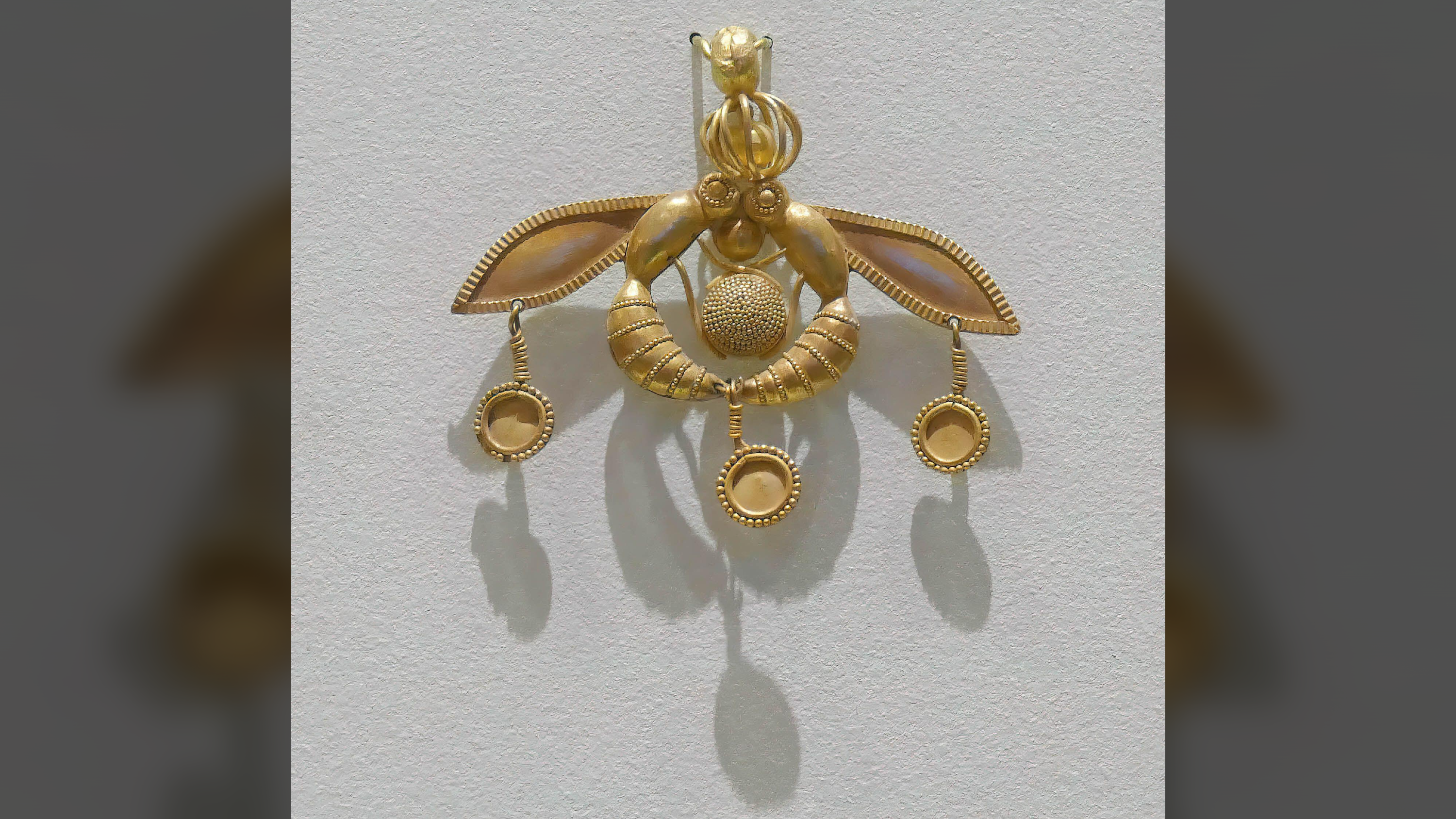 Un pendentif en or en forme de deux insectes face à face avec trois cercles d'or qui se balançaient, sur un fond gris clair