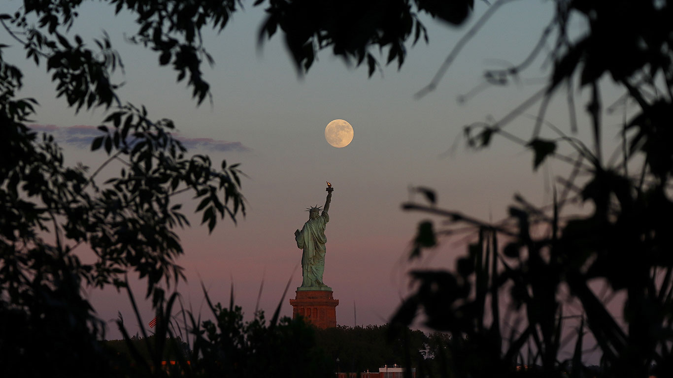 Une presque pleine lune s'élève au-dessus de la statue de la liberté alors que le soleil se couche à New York le 23 juin 2021 vu de Jersey City, New Jersey.