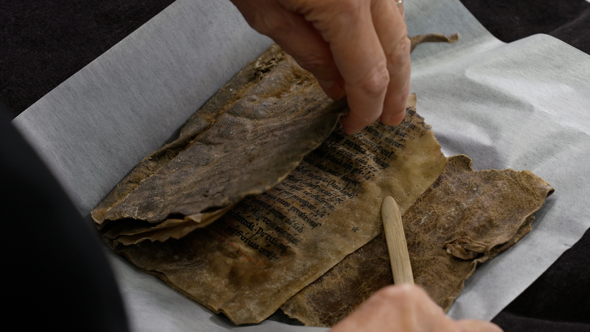 a person opens a medieval manuscript and places a wooden pointer on it