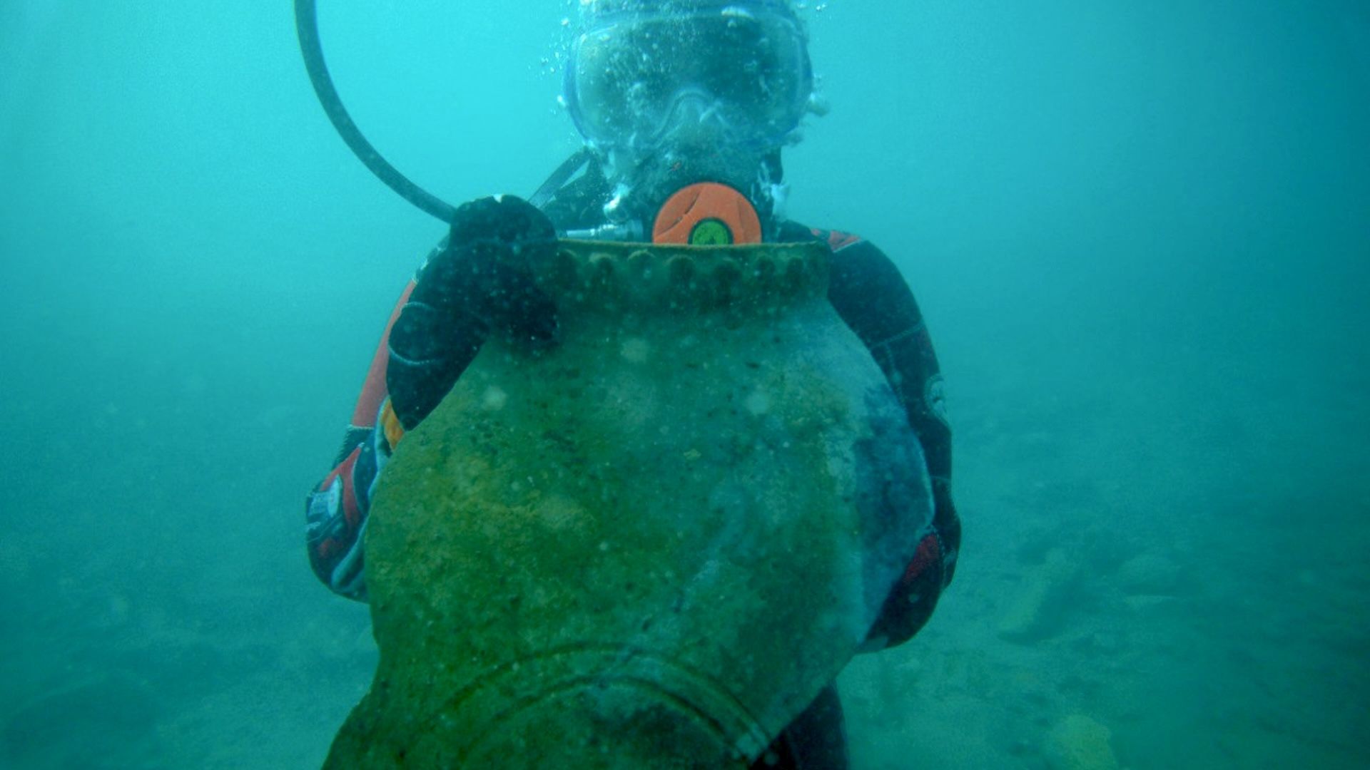 a researcher in scuba gear holds up a large ceramic fragment underwater