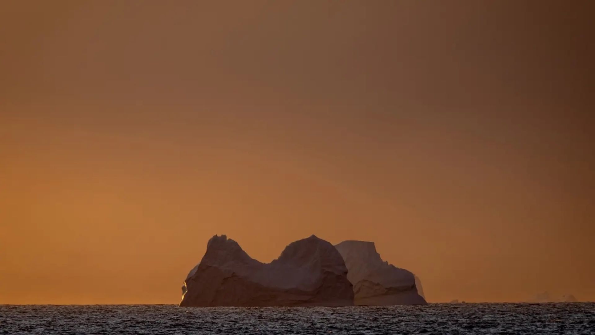 a view of a glacier in the ocean with an orange sky behind it