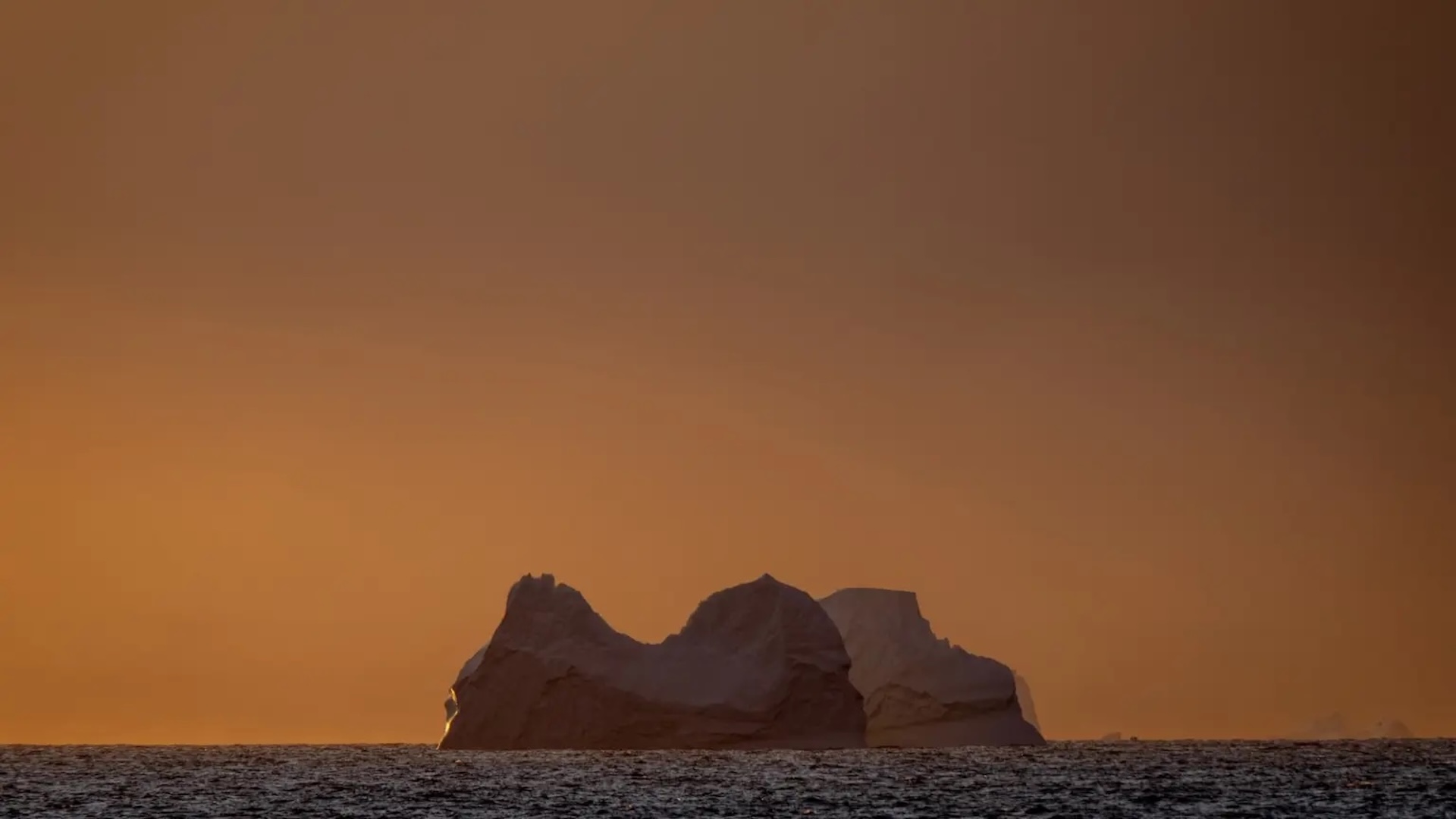 une vue d'un glacier dans l'océan avec un ciel orange derrière lui