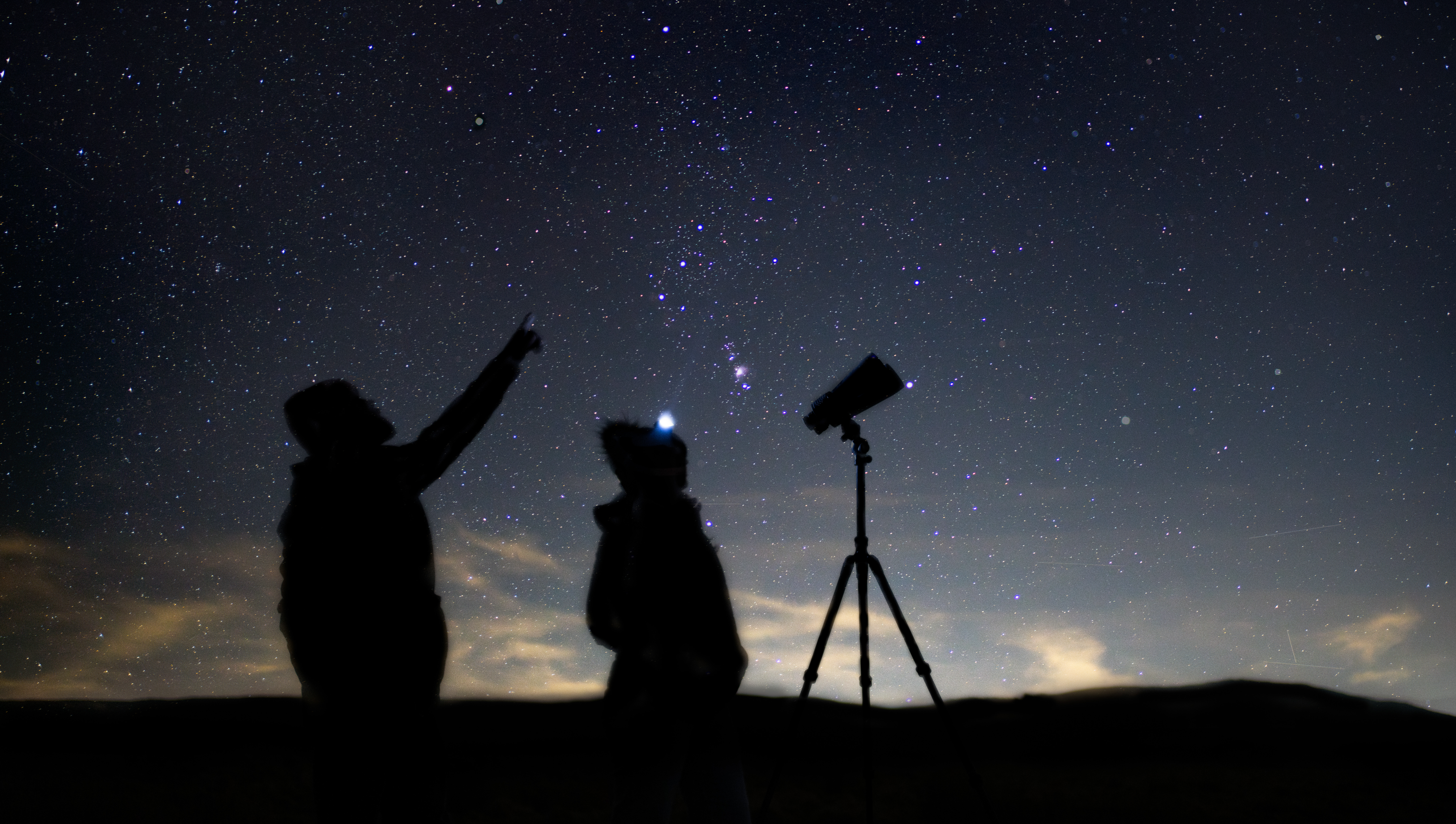 deux personnes se tenaient à côté de jumelles montées sur trépied contre le ciel nocturne
