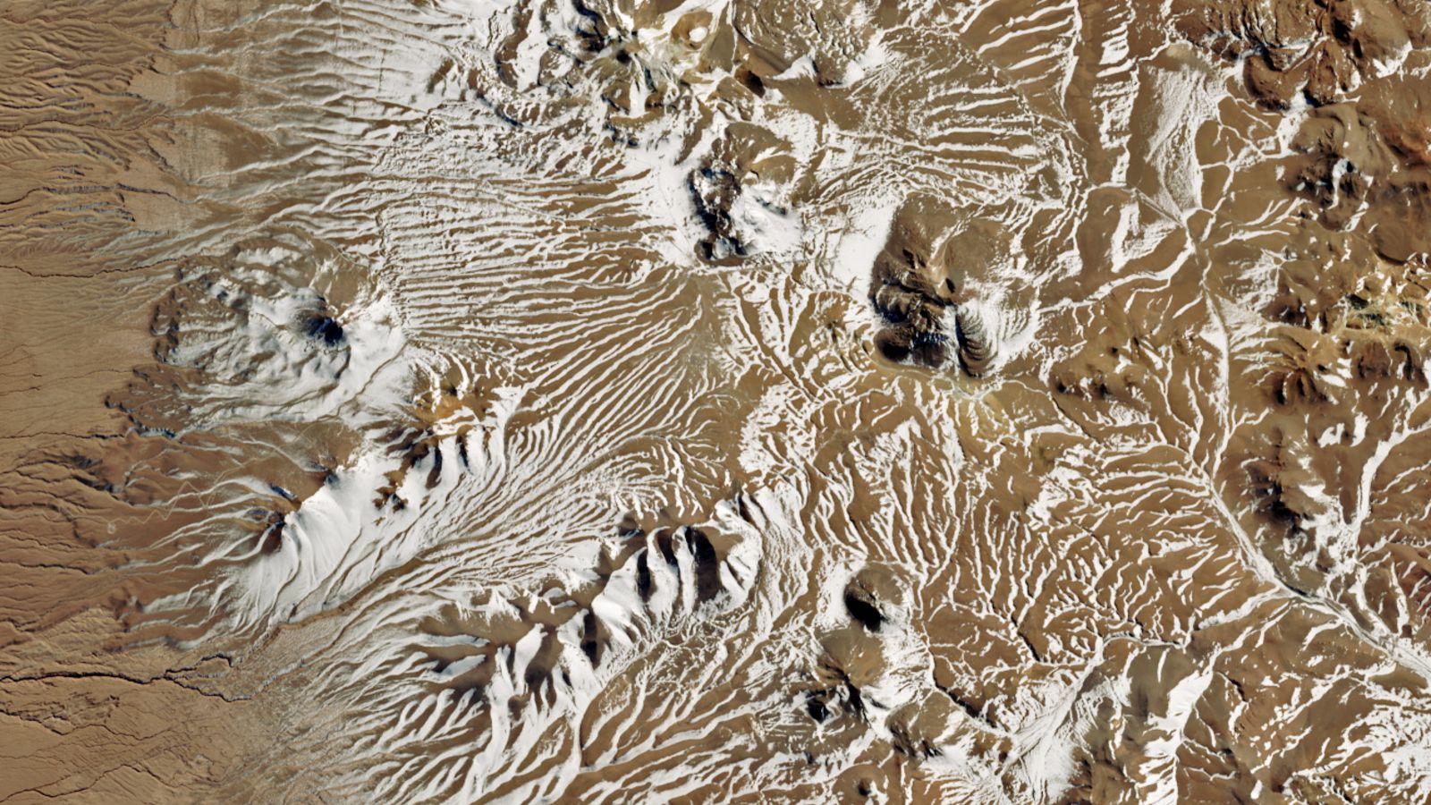 A satellite photo of a desert covered in streaks of white snow