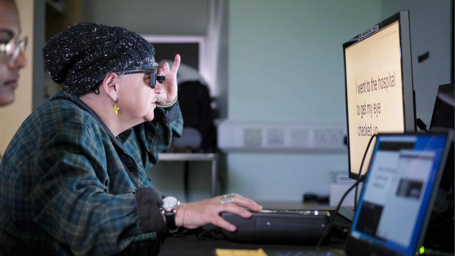 une photo d'une femme âgée portant des lunettes de réalité augmentée pour lire des mots sur un écran d'ordinateur