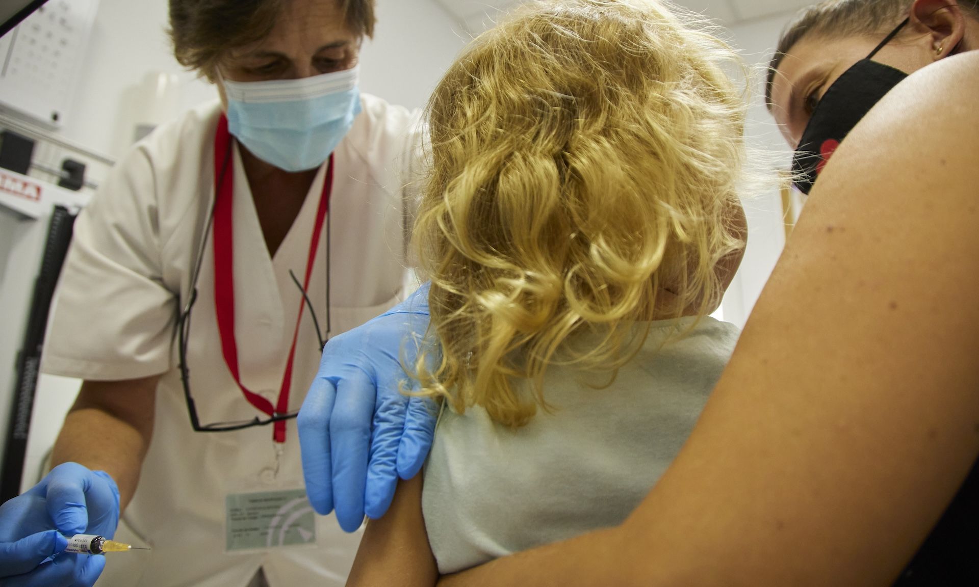 A child being held by her mother prepares to get a vaccine at a doctor's office