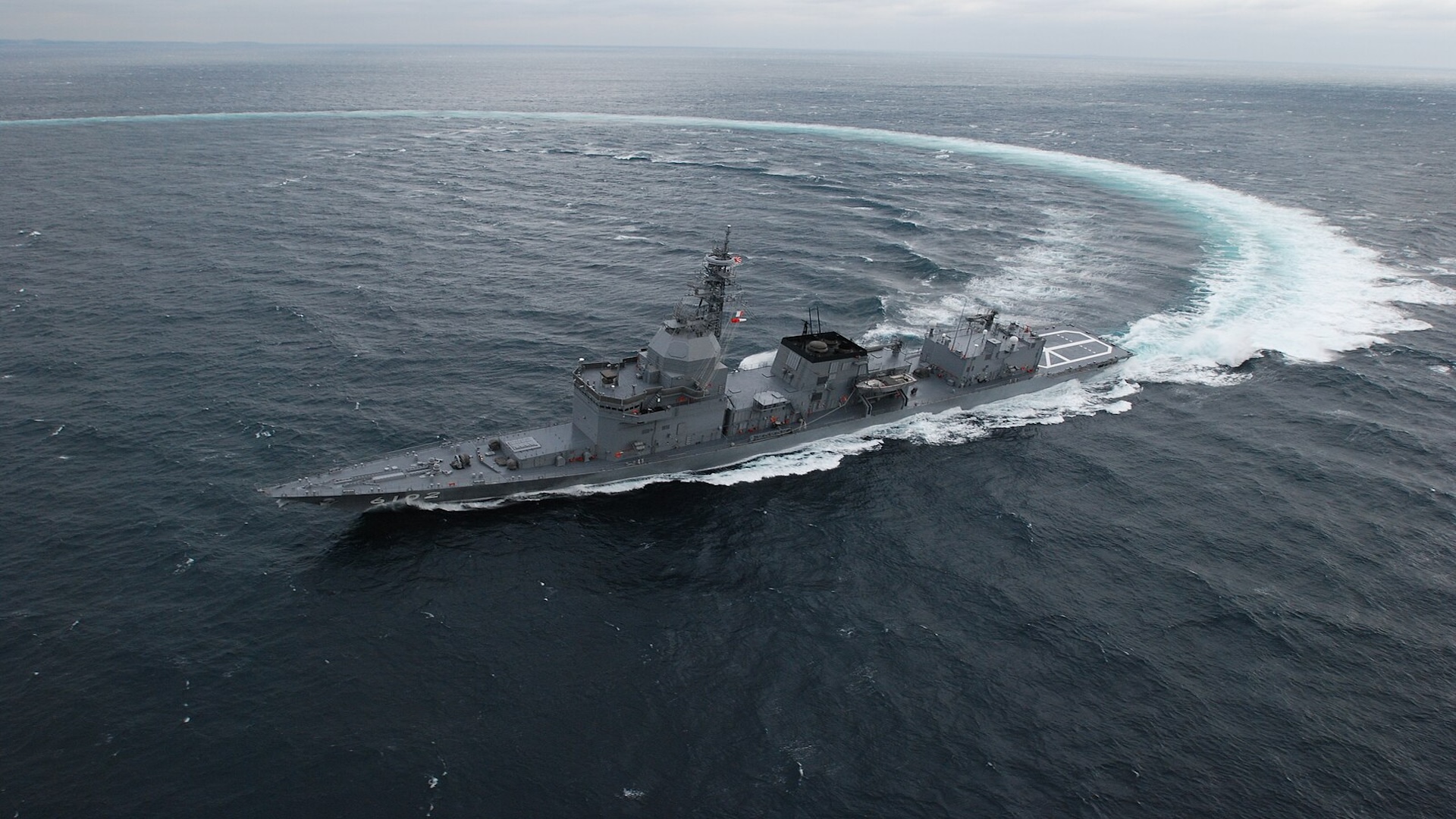 Photographie aérienne du navire japonais JS Asuka effectuant une manœuvre de virage dans l'océan. 