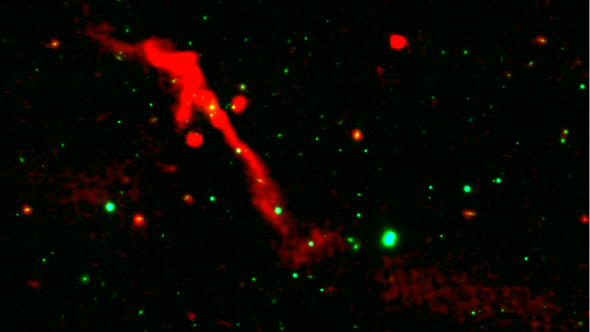 A red ribbon of radio energy blasts out of a black hole on a black background