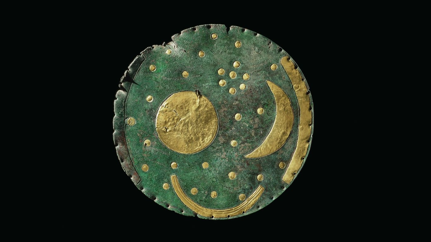 un disque en bronze à patine verte avec des accents dorés représentant un croissant de lune, un soleil et un bateau