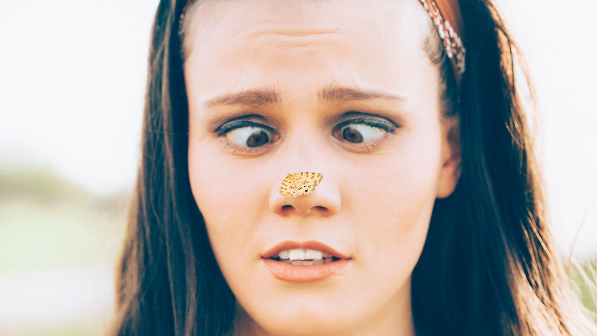 Photo du visage d'une personne alors qu'elle regarde, les yeux croisés, un petit papillon jaune posé sur le bout de son nez. 