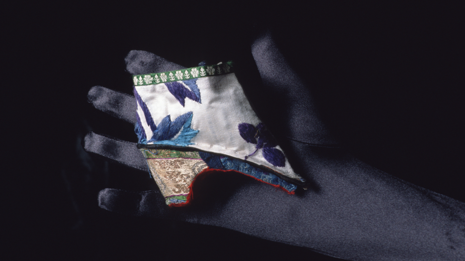 a person with a dark glove holds a very small heeled shoe