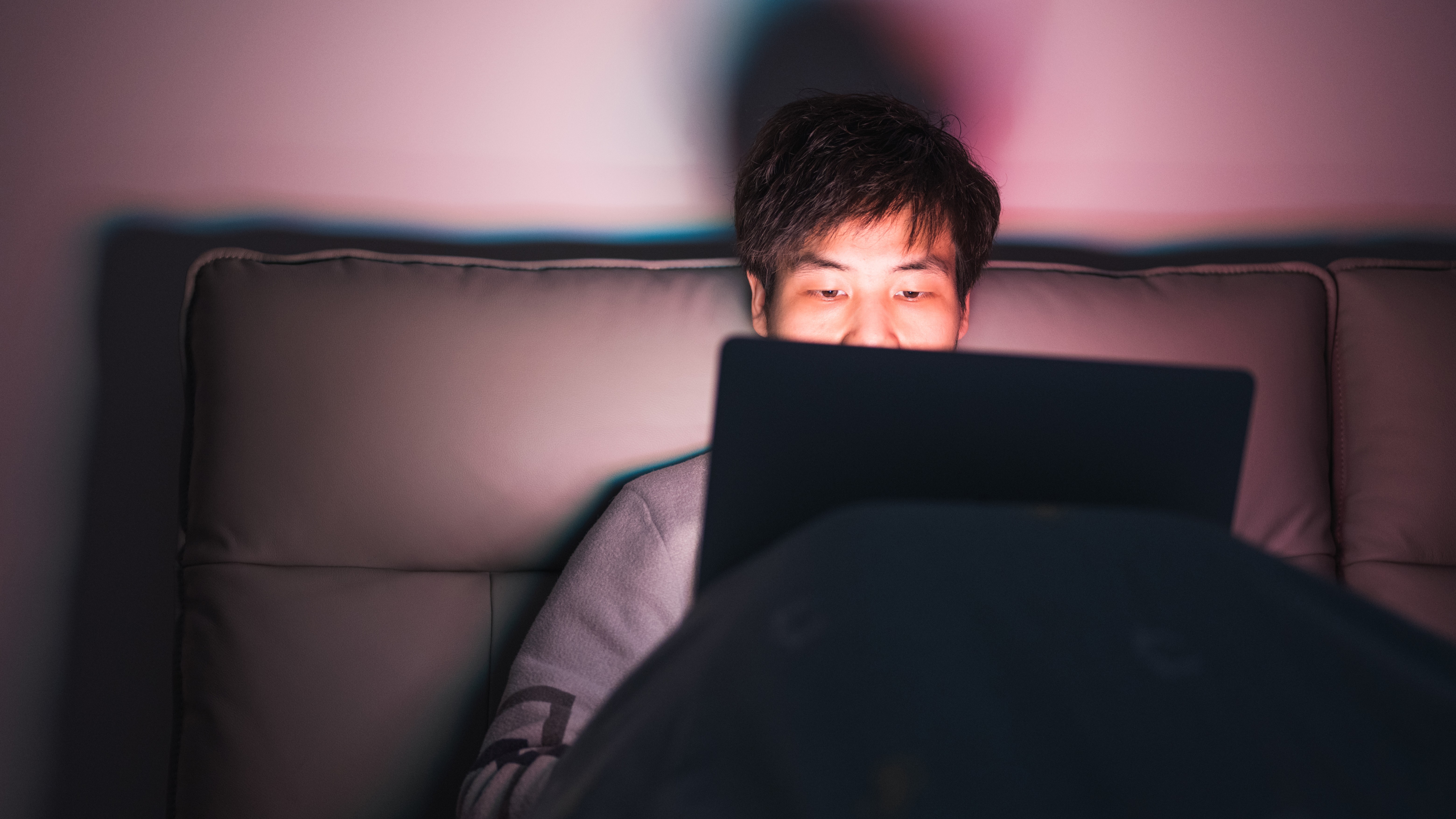 un homme assis dans son lit travaillant sur un ordinateur portable