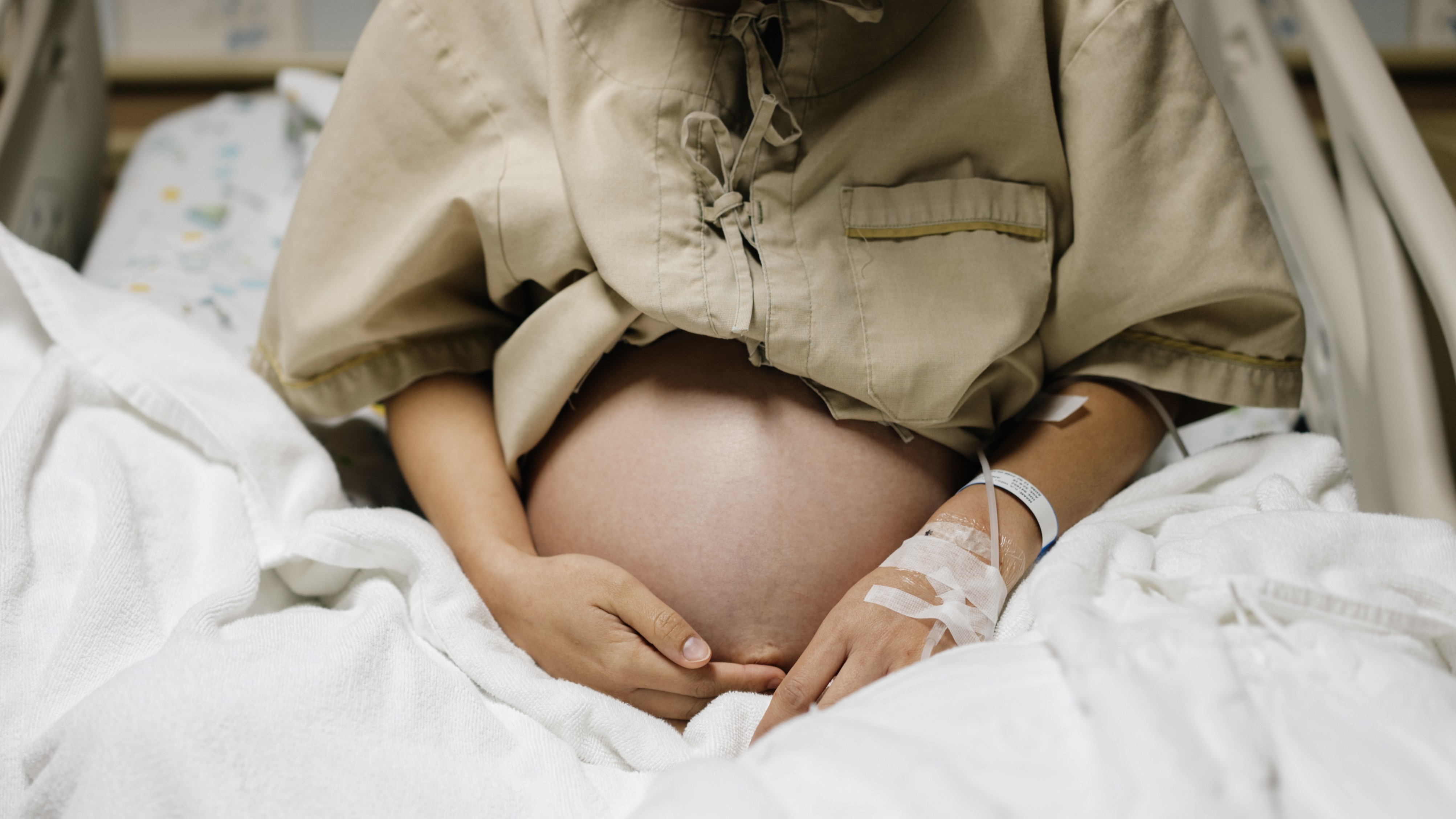 photo du ventre d'une femme enceinte alors qu'elle est assise sur un lit d'hôpital avec une intraveineuse à la main