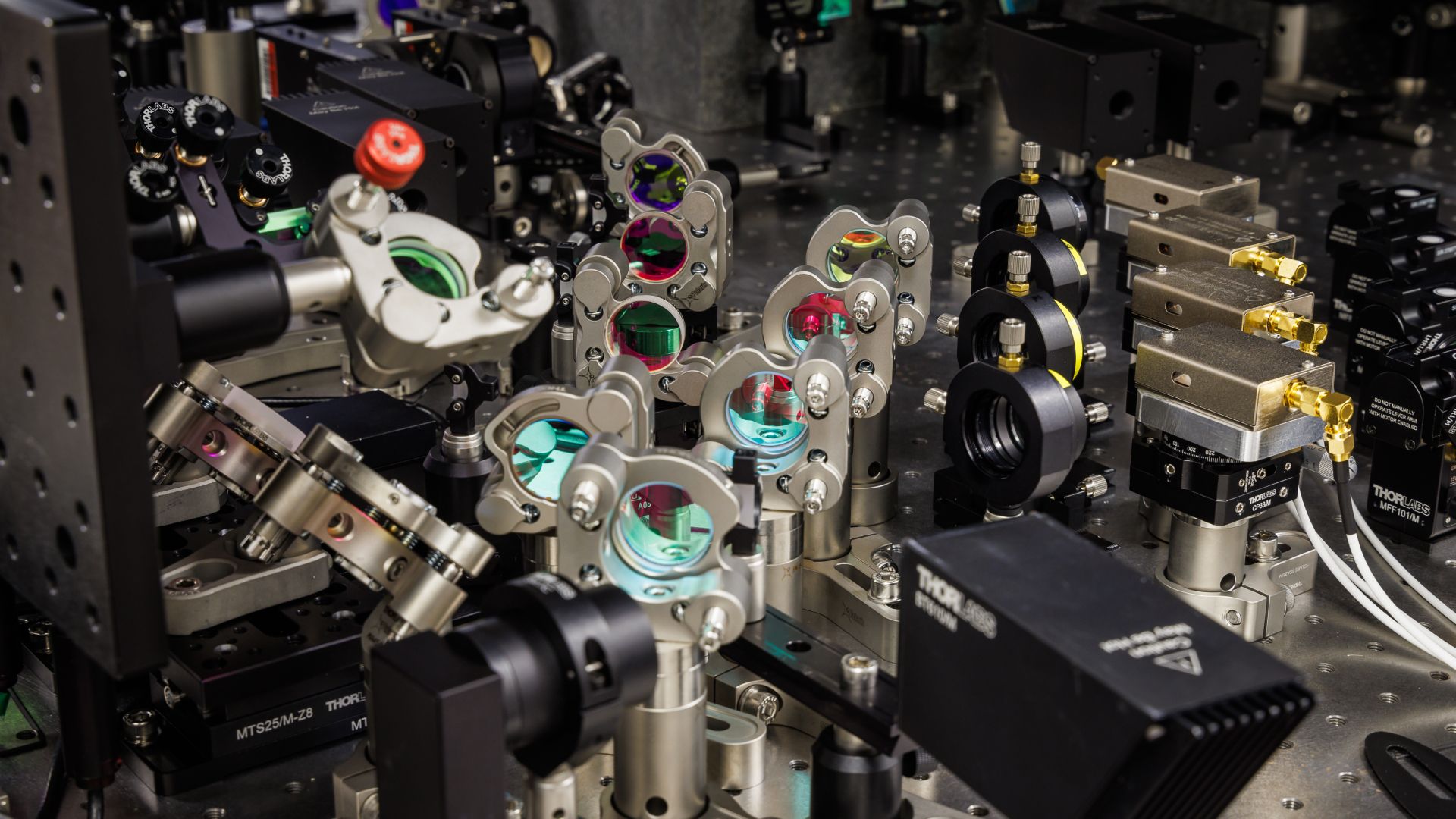 A close up of an array of lenses, mirrors and lasers sitting on a table