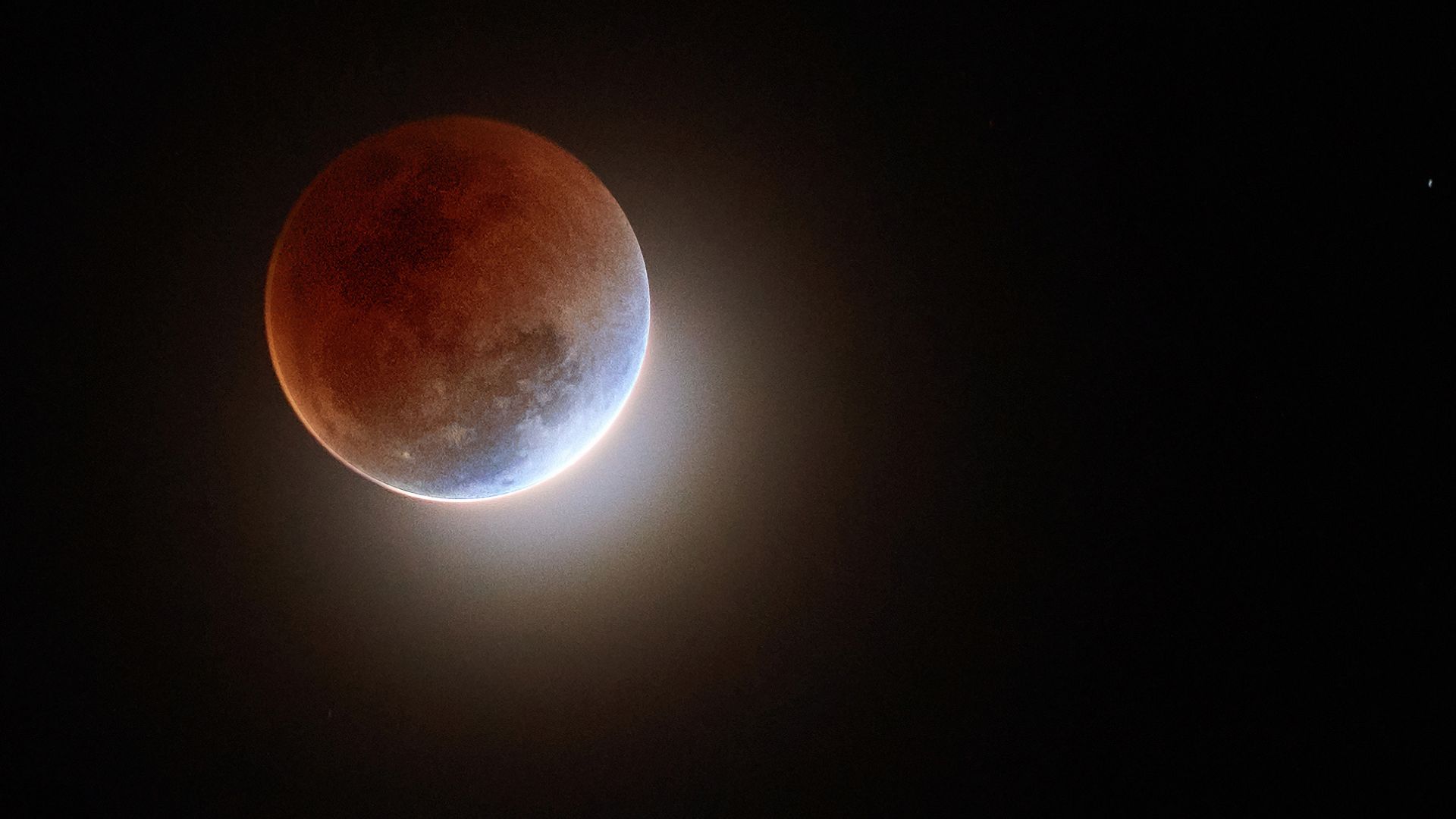 Image d'une lune teintée de rouge sur un ciel noir et clair avec un petit anneau de lumière sortant du coin inférieur droit de la lune. 