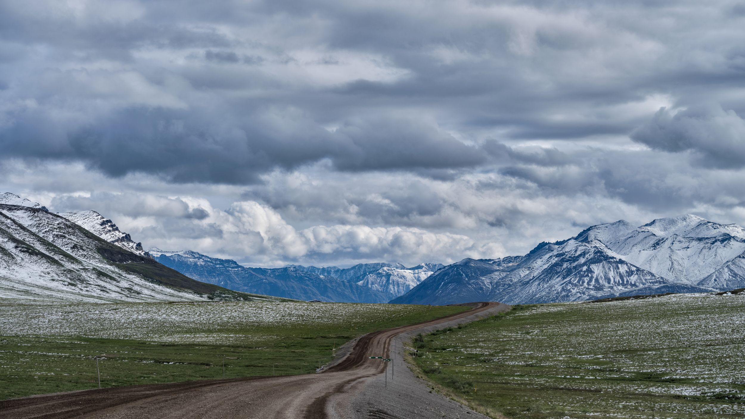longue route le long de la toundra avec des montagnes en arrière-plan et un ciel nuageux