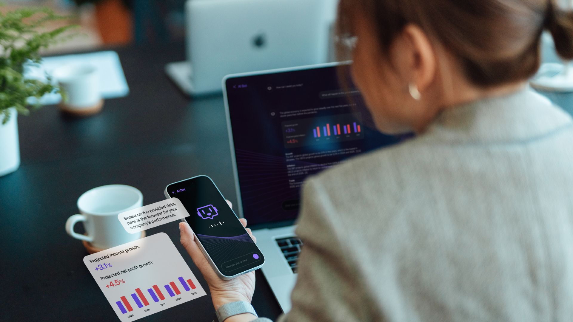 A woman with dark hair in a pony tail wearing a gray blazer looks at both a laptop and phone both displaying various bar charts.