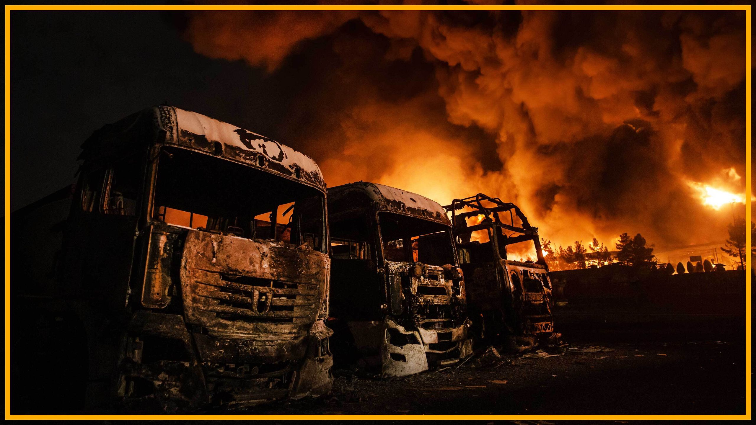 burnt out trucks with fire in the background of an oil depot