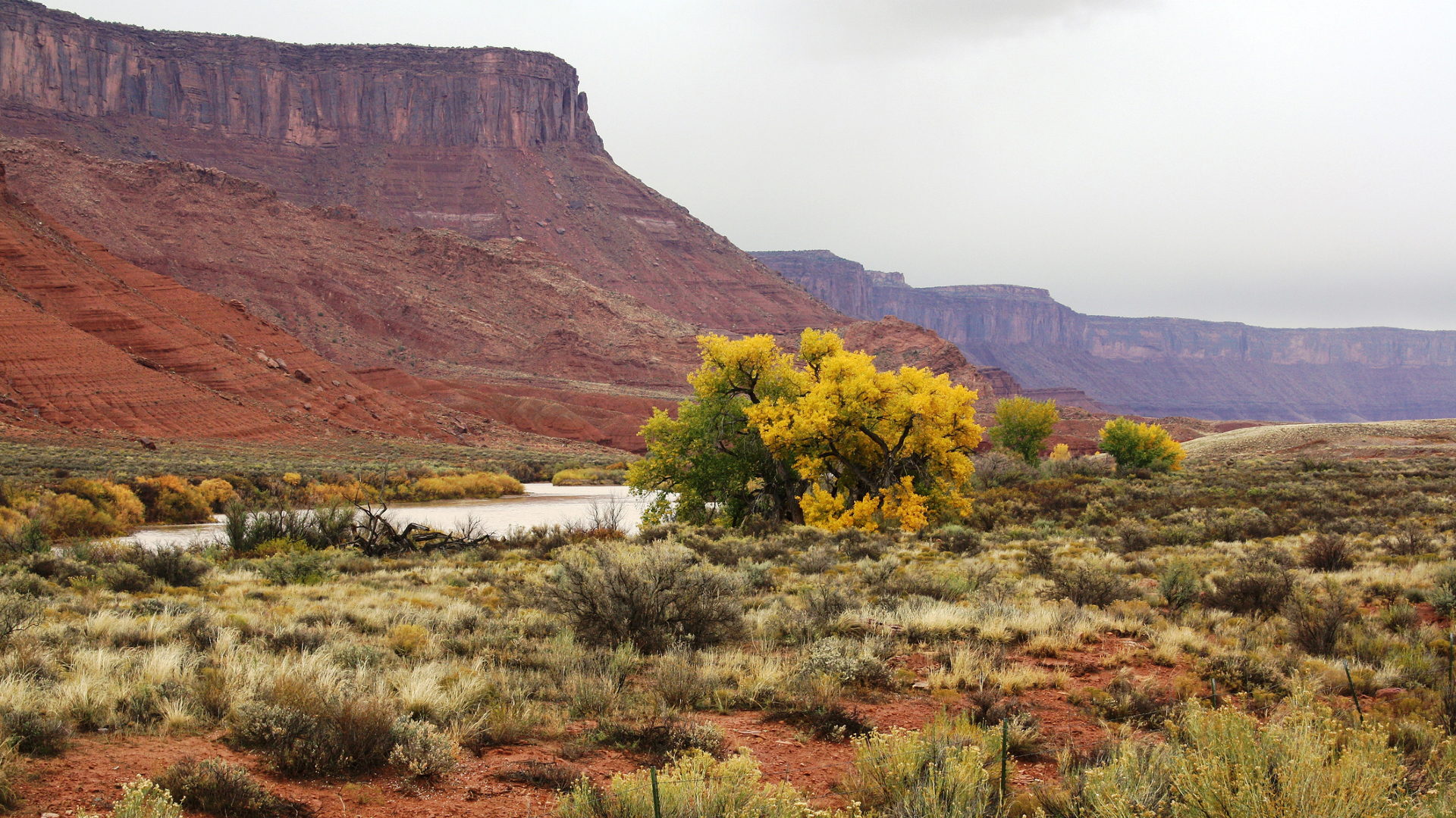 Une plus grande butte rougeâtre surplombe une rivière qui coule avec de la sauge et des broussailles de chaque côté