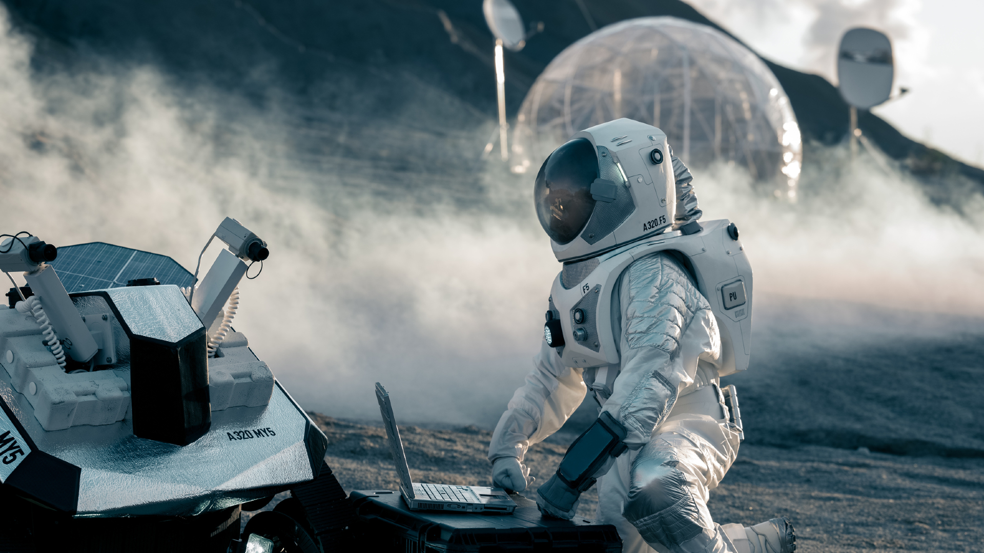 Un astronaute portant une combinaison spatiale blanche s'agenouille devant un ordinateur connecté à un rover sur la surface poussiéreuse de la lune avec une boule circulaire transparente derrière lui.