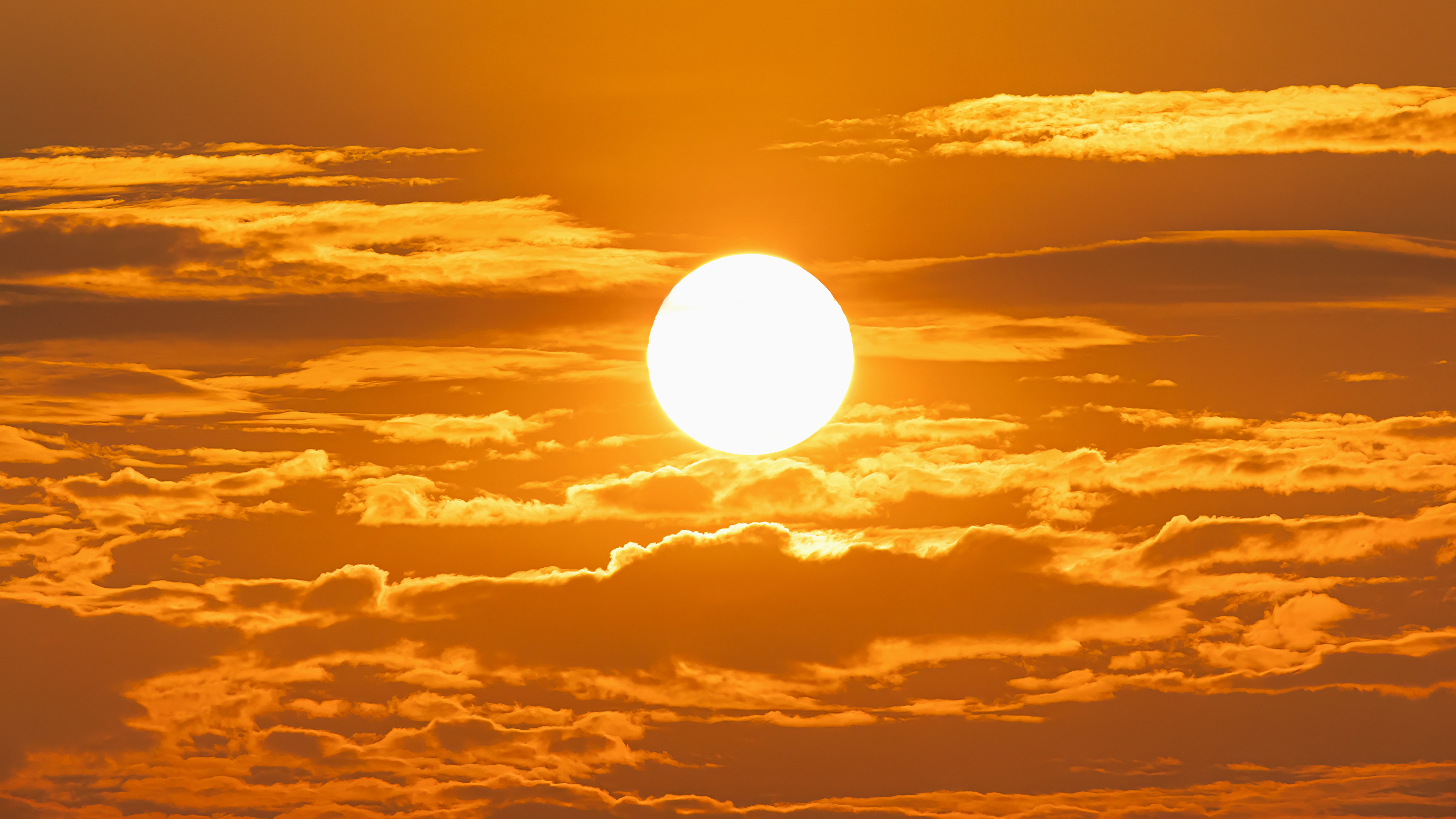 Une photo du soleil se levant au-dessus des nuages ​​dans un ciel orange. 