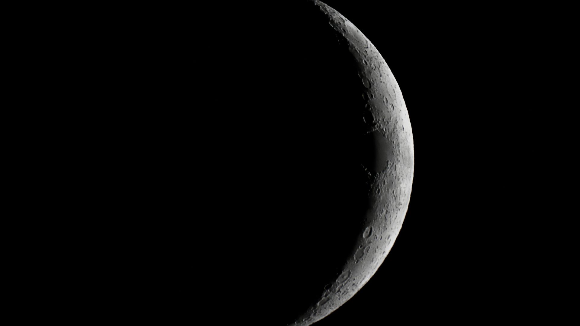 A close up of the moon in the darkness of space, with only it's right outer edge illuminated by the sun.