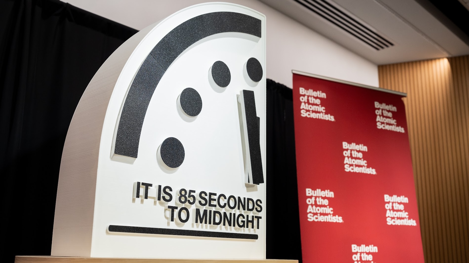 Une présentation montrant une partie d'une horloge à minuit moins 85 secondes à côté d'une bannière rouge du Bulletin of the Atomic Scientists. 