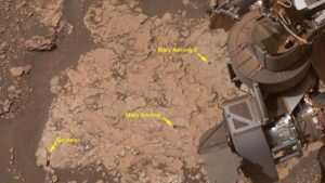 A close up of a reddish brown surface with a metal arm in the right top corner of the image. The image includes yellow arrows and labels of different sites of interest.
