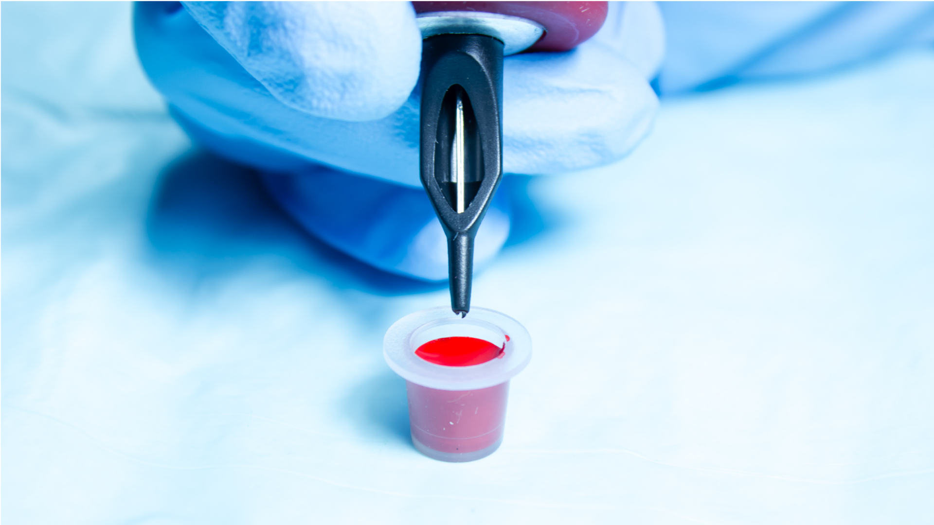 Une personne tenant des aiguilles de tatouage avec un pot d'encre rouge.