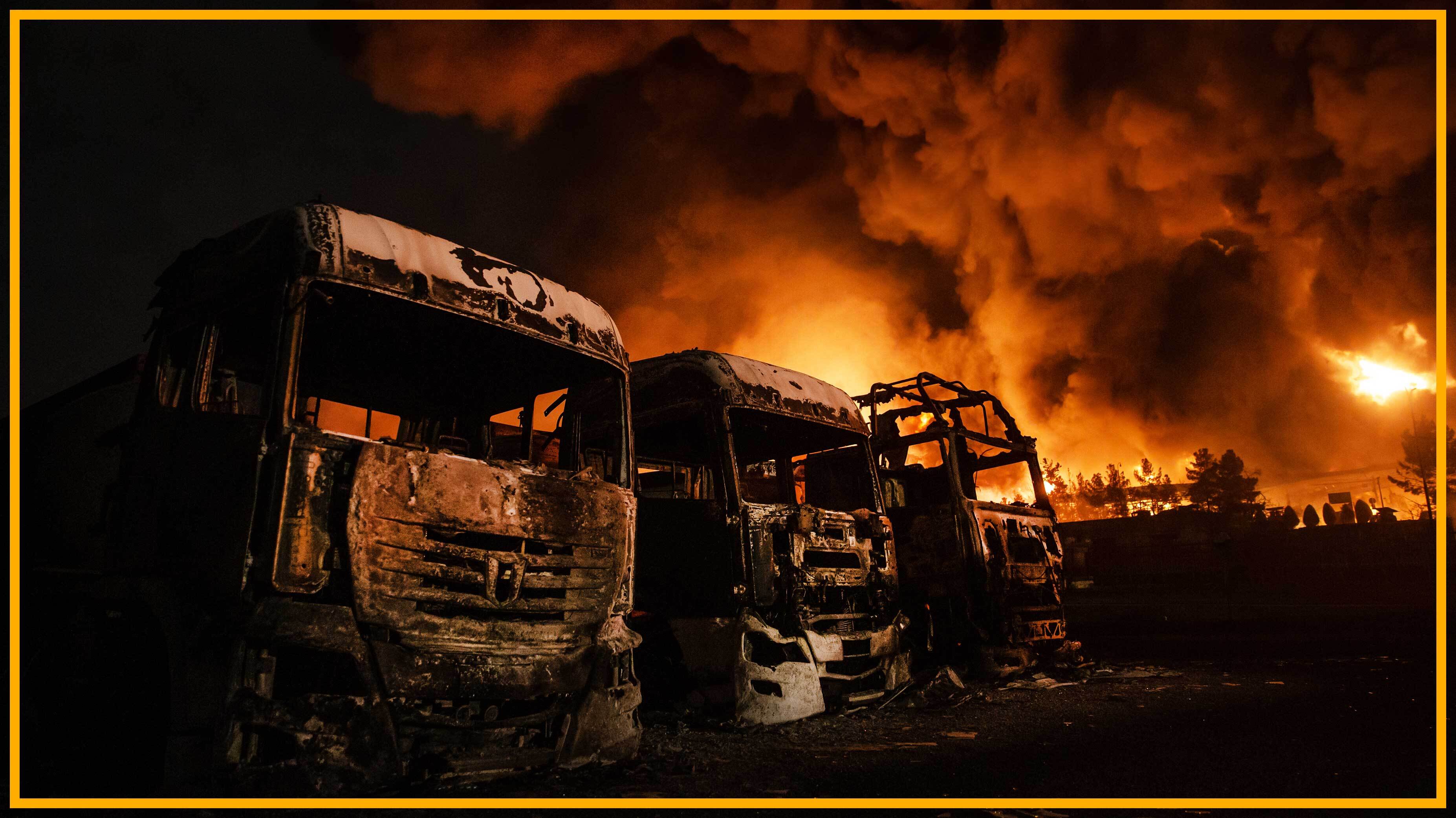 camions incendiés avec le feu en arrière-plan d'un dépôt pétrolier