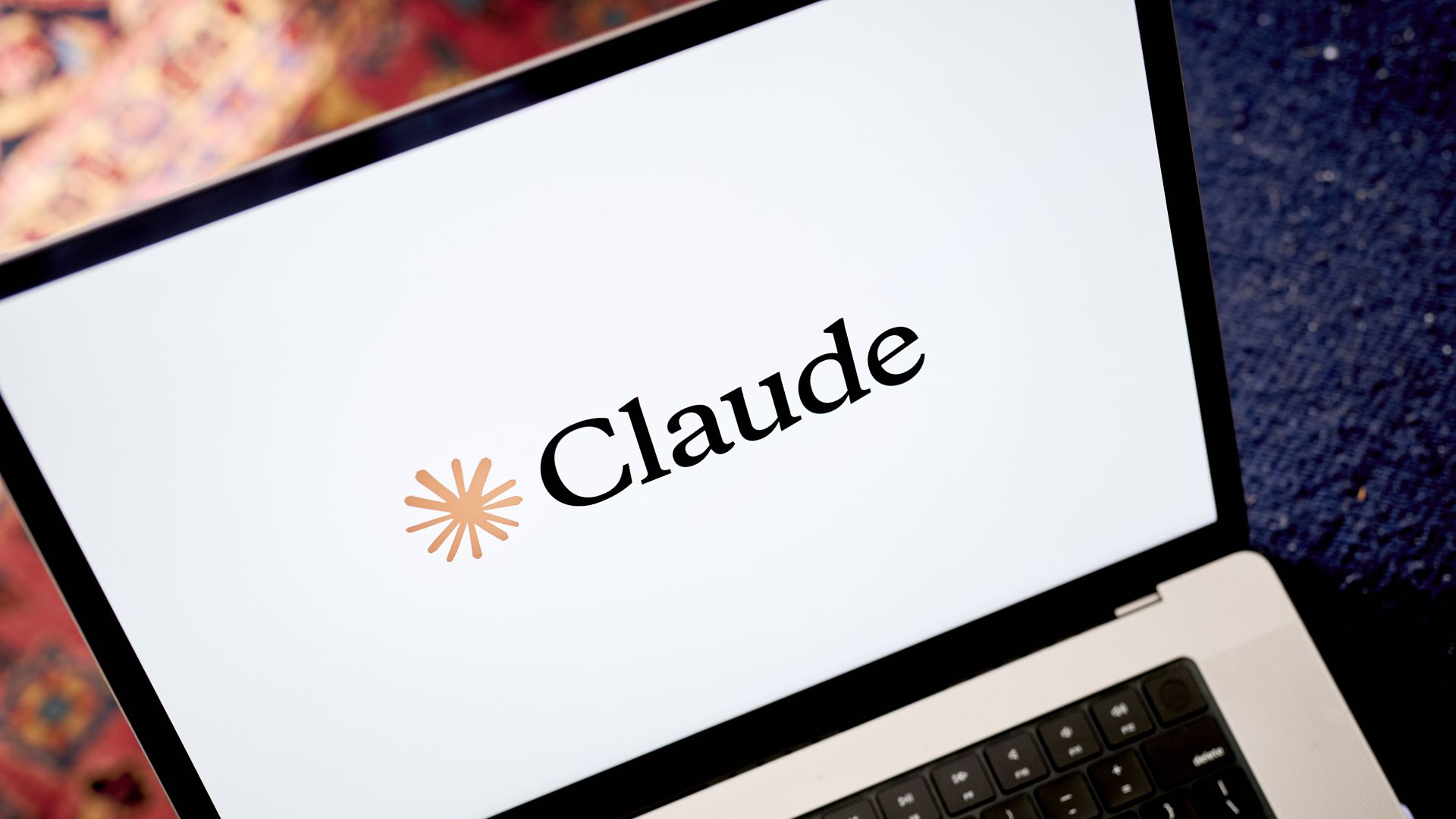 A close up of a laptop showing a white screen with the word "Claude" on it in dark black letters