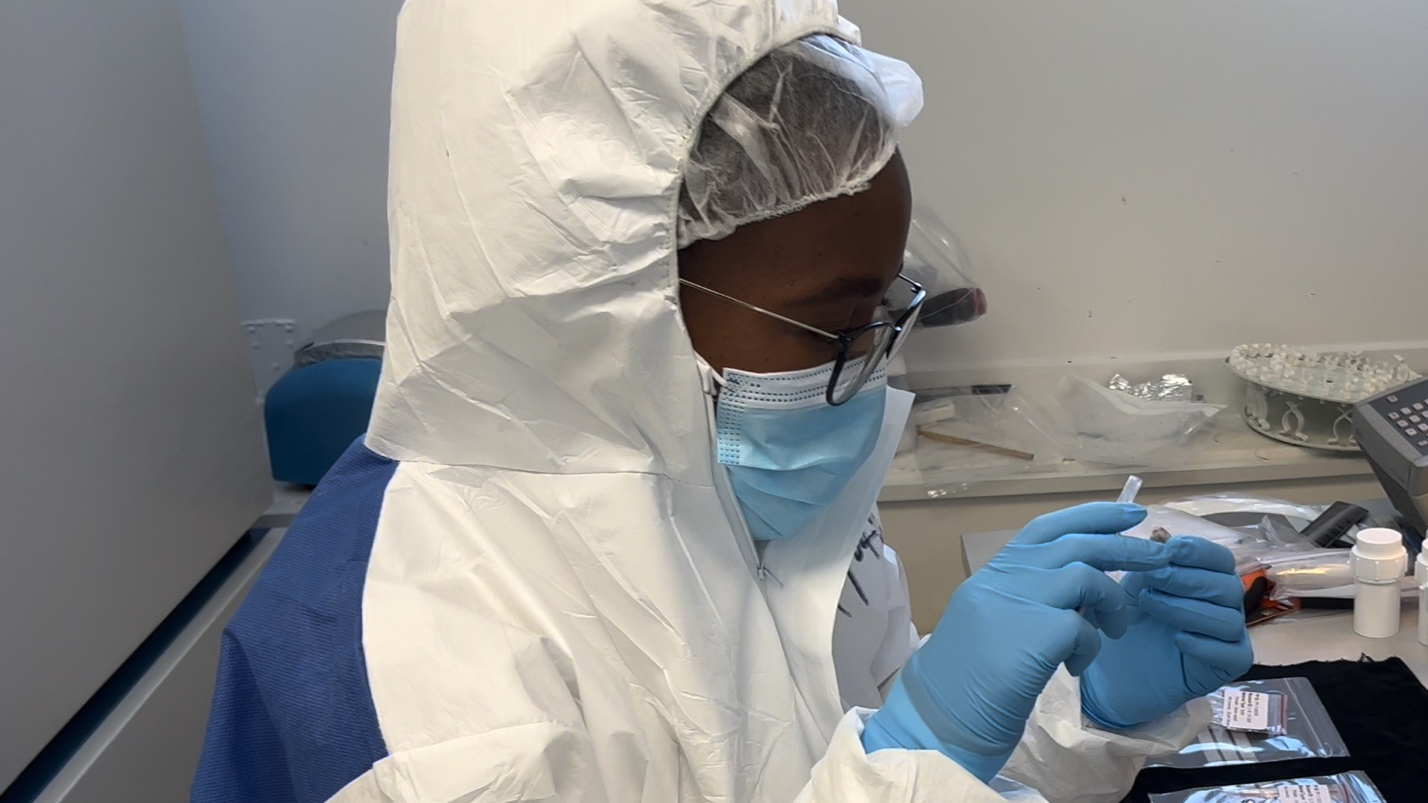 un scientifique à la peau foncée et aux lunettes porte une blouse blanche et des gants bleus pour tester quelque chose