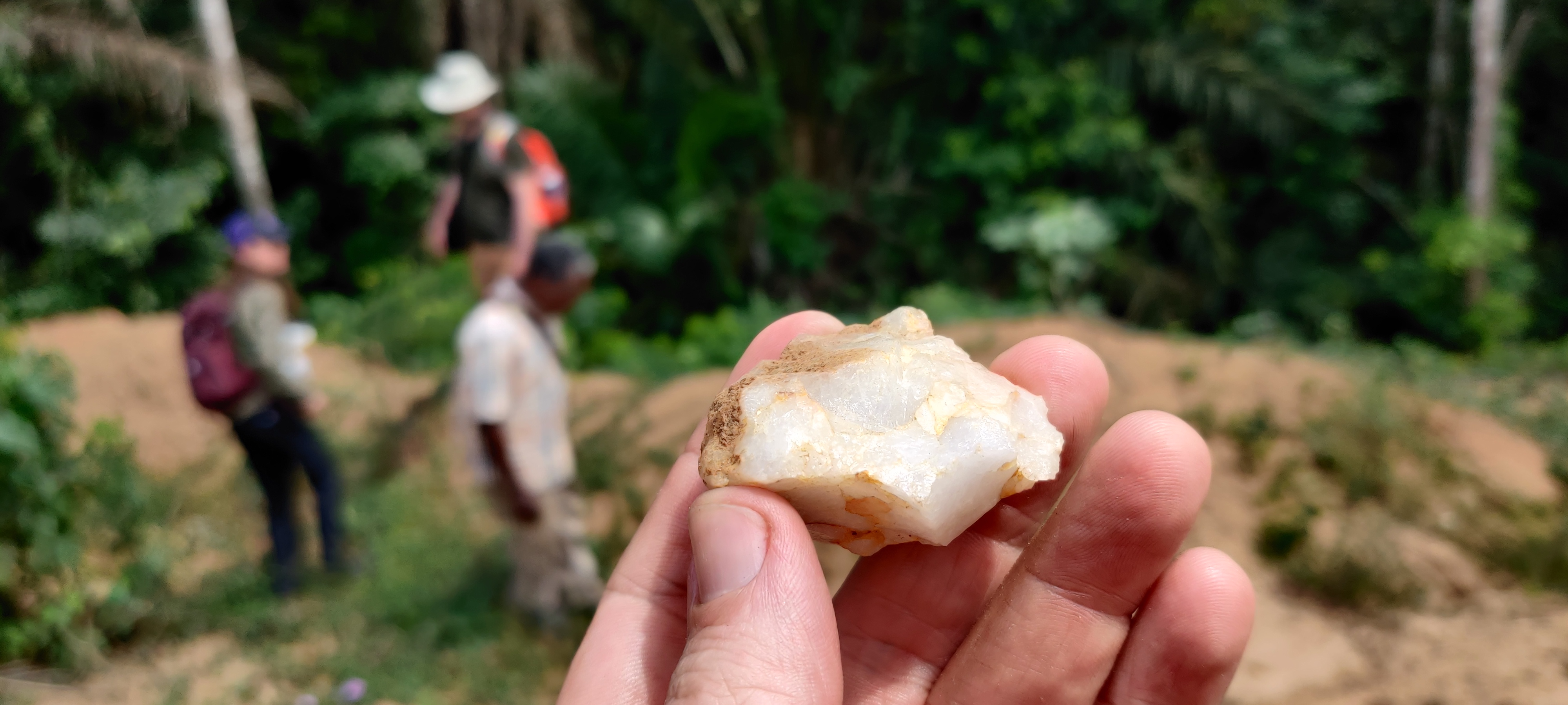 Petit outil à quartz tenu à la main avec des archéologues travaillant en arrière-plan