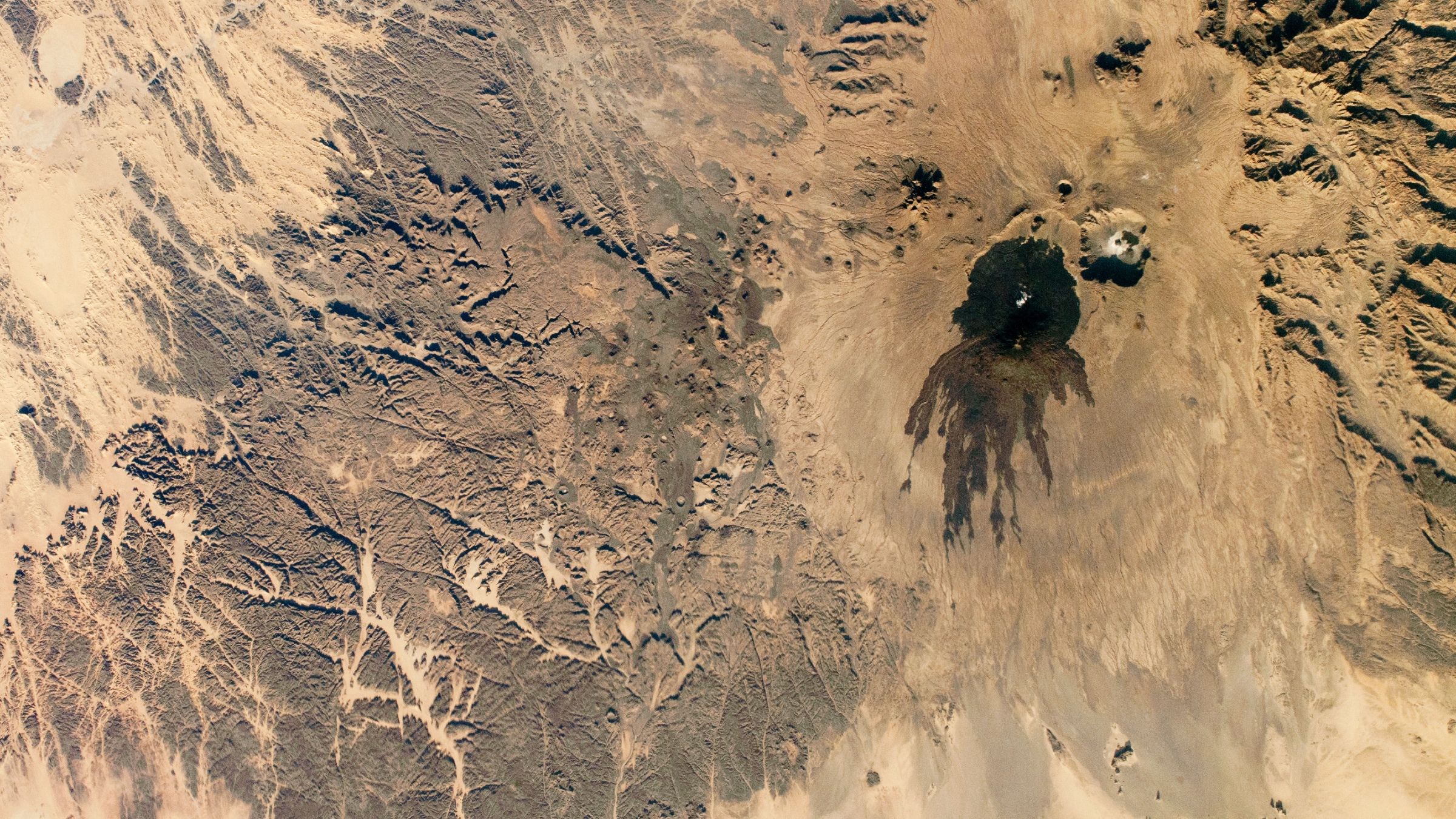 Des vrilles sombres de lave ancienne ont marqué un volcan sombre à côté d'un "crâne" dans le Sahara — La Terre vue de l'espace