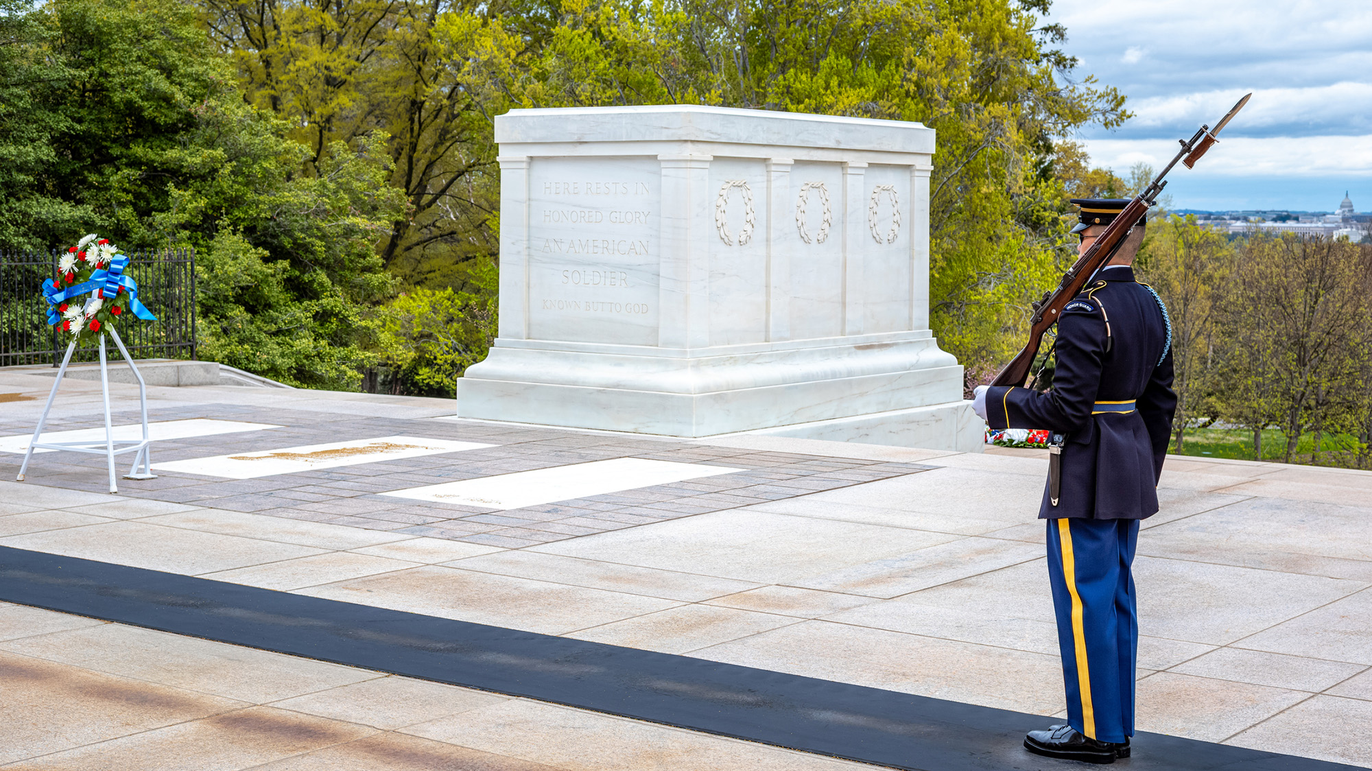 Un homme en uniforme, un fusil sur l'épaule gauche, se tient au milieu d'un grand monument.