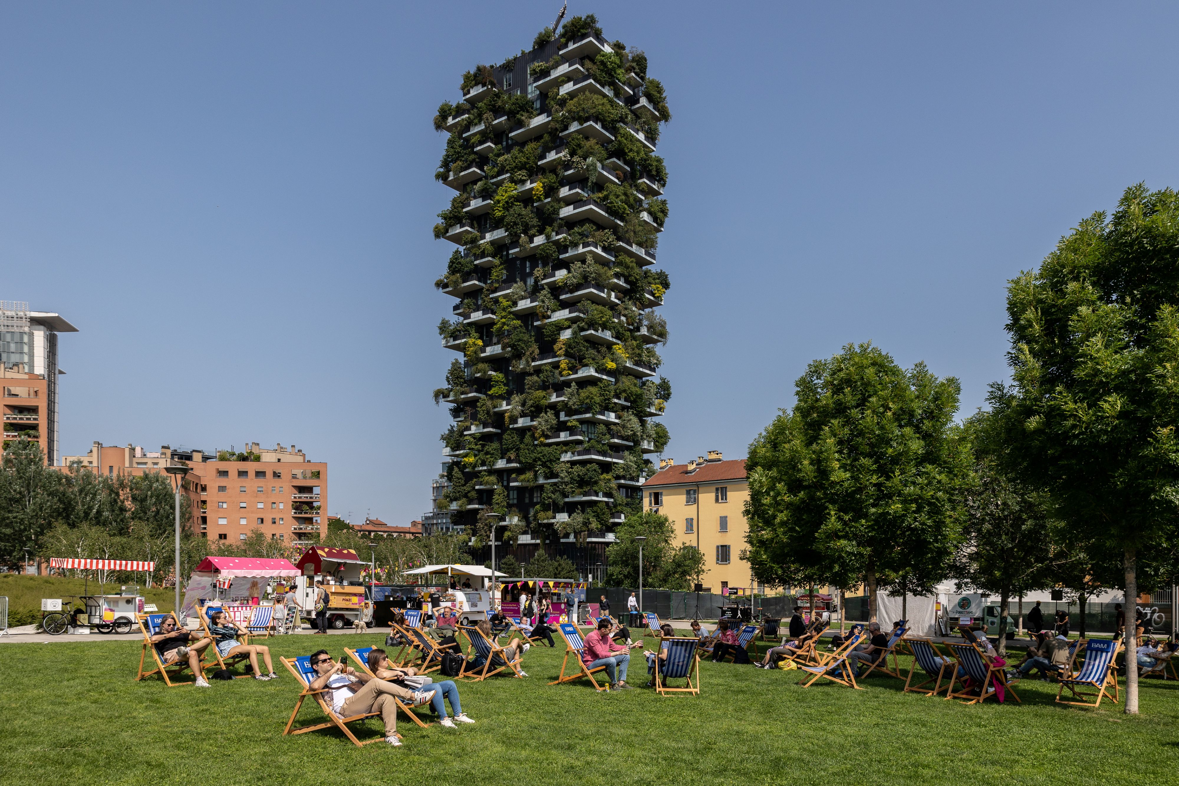 un parc à Milan avec des gens sur des chaises longues et un immeuble de grande hauteur couvert de plantes