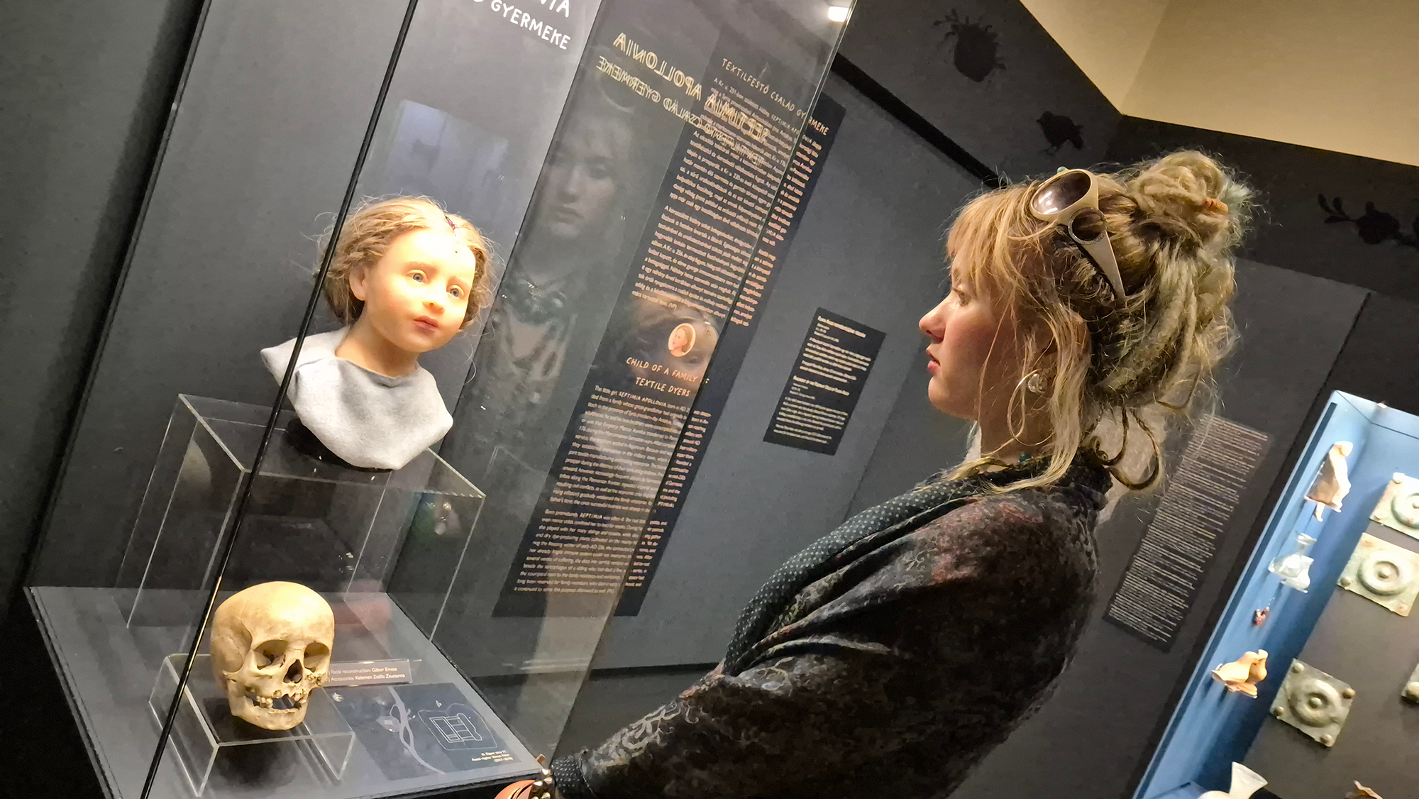 Une femme se tient devant une vitrine en verre montrant un jeune visage et un crâne devant elle