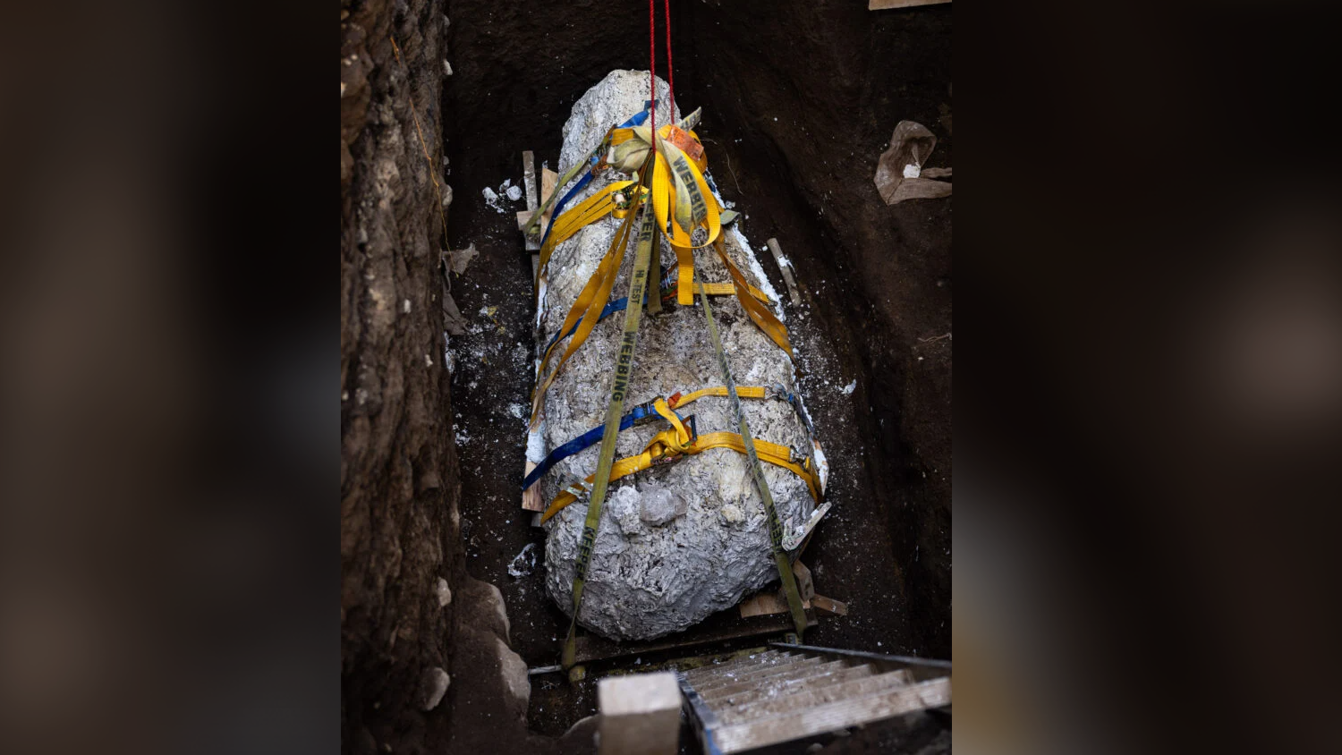 un paquet de plâtre blanc est tiré d'un fossé profond au moyen de sangles jaunes