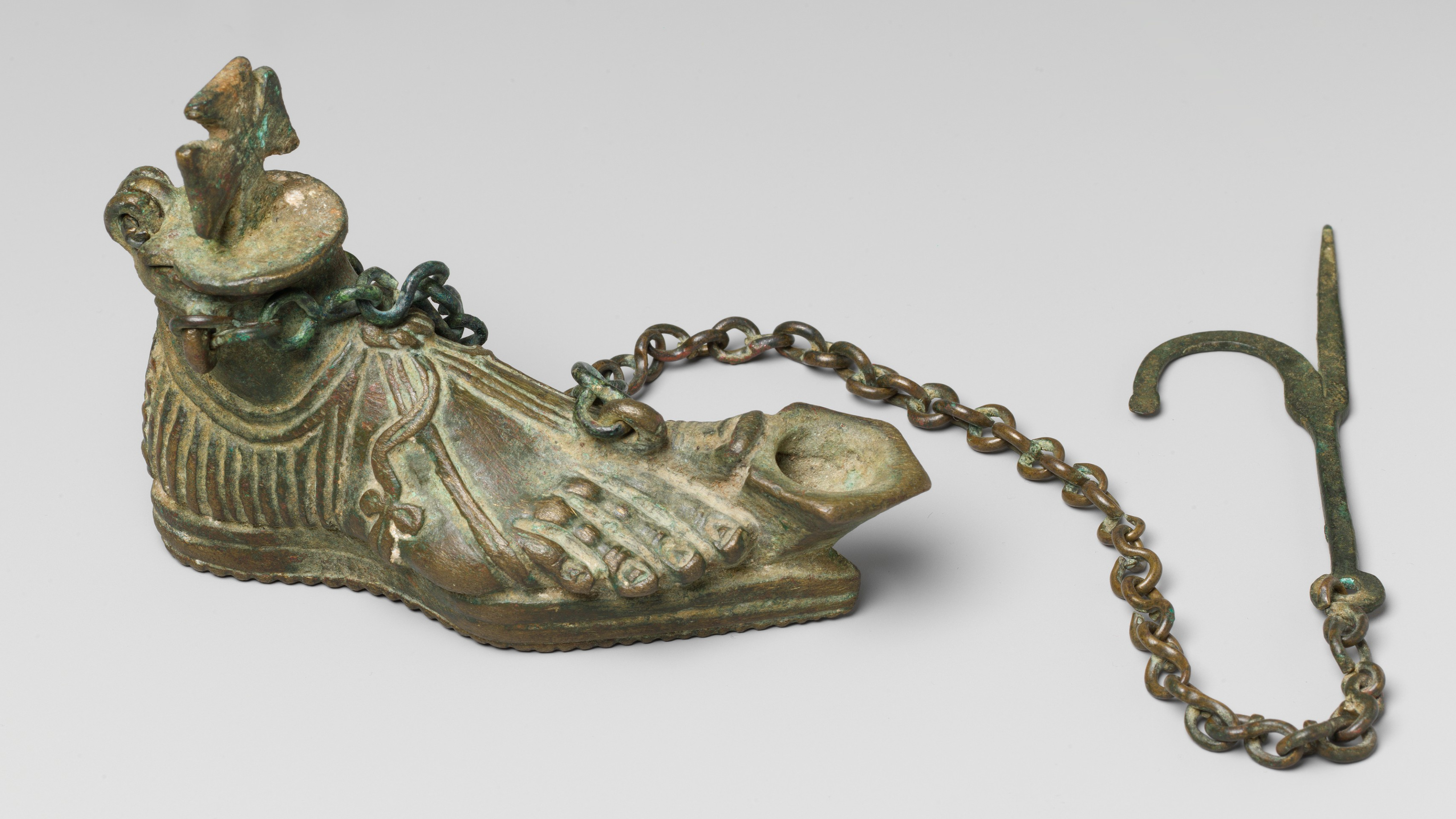 une lampe à huile en bronze en forme de pied avec une chaîne suspendue