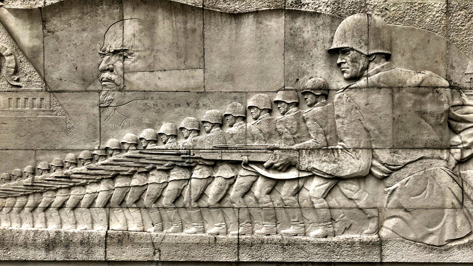 Une sculpture murale représentant des soldats portant des casques circulaires et des fusils.