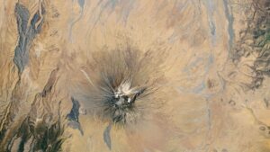 Satellite picture of a dry region with a volcano capped with white ash