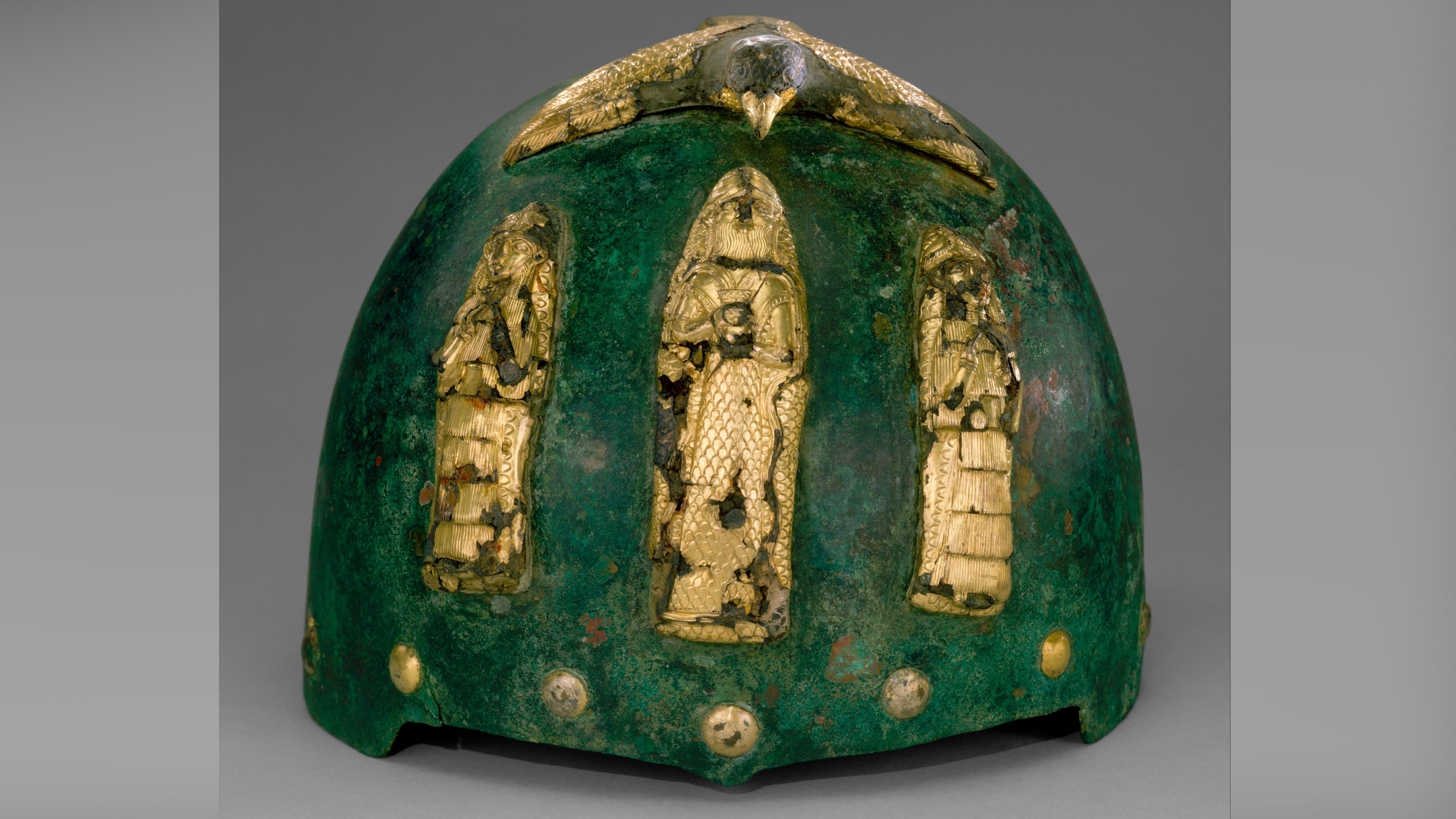 un casque en bronze teinté vert avec des figurines dorées sur le devant