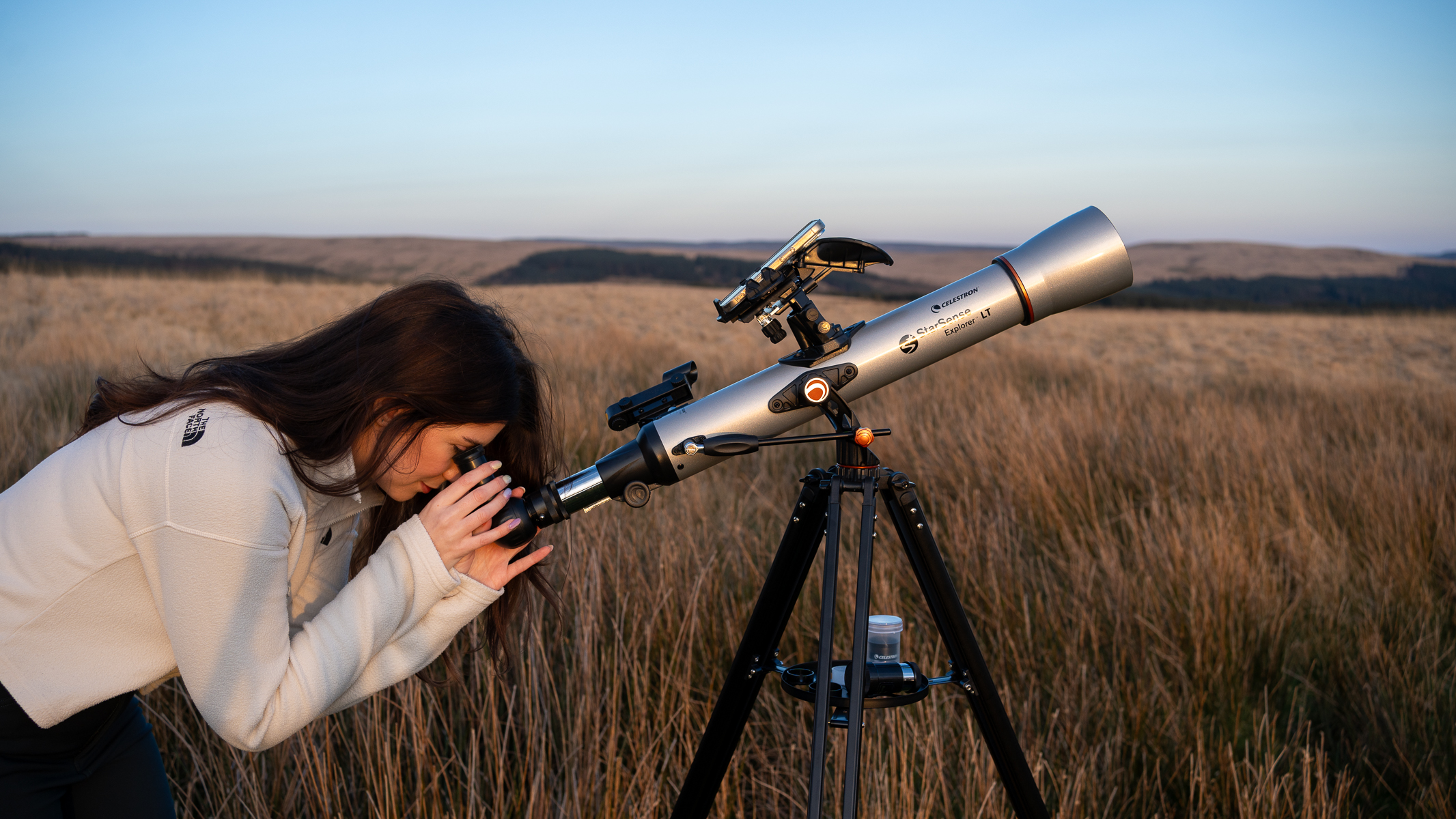femme vêtue d'un haut blanc regardant à travers le Celestron StarSense Explorer LT 70AZ