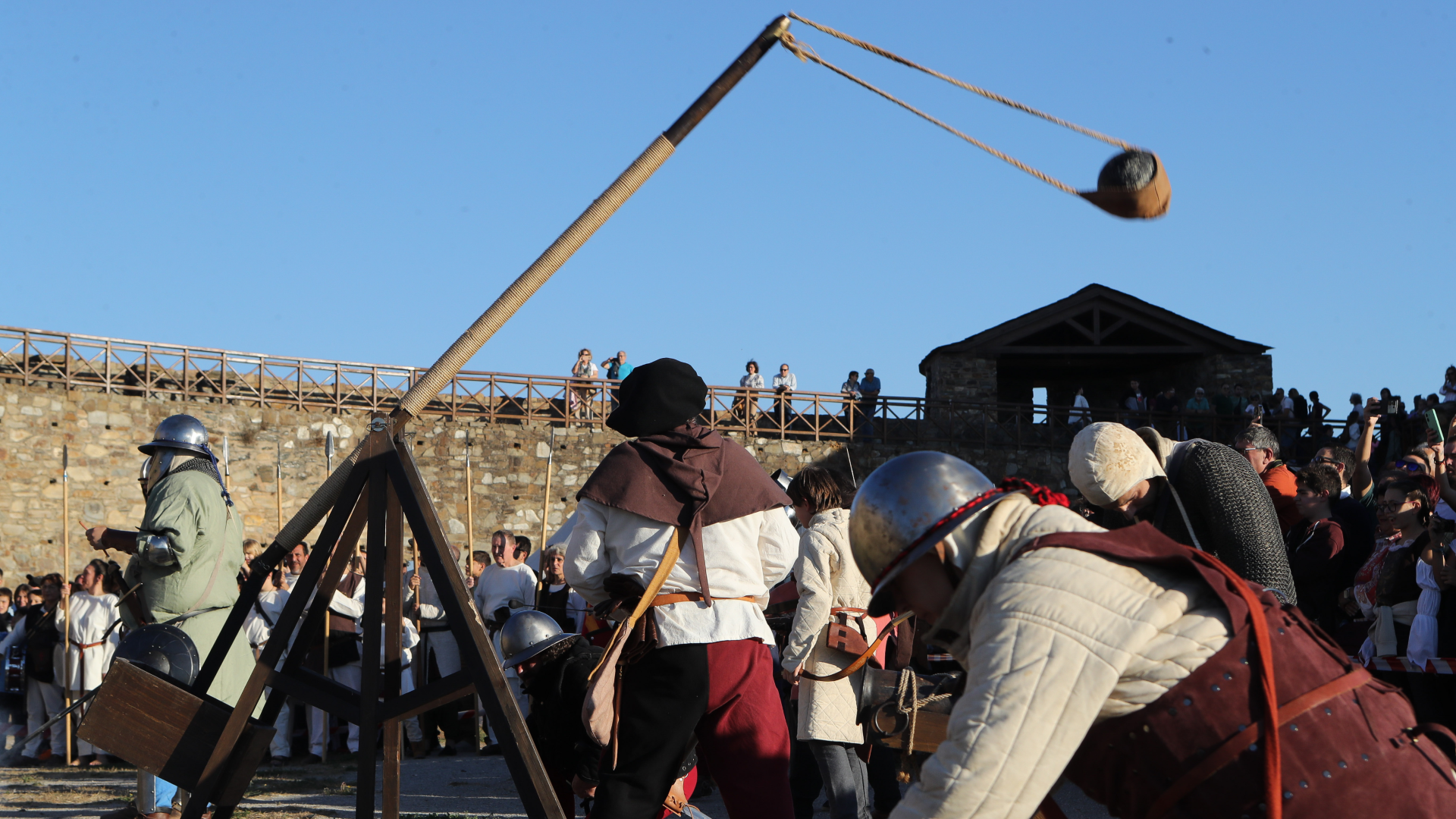 reenactors dressed in medieval garb shoot at trebuchet at a castle wall