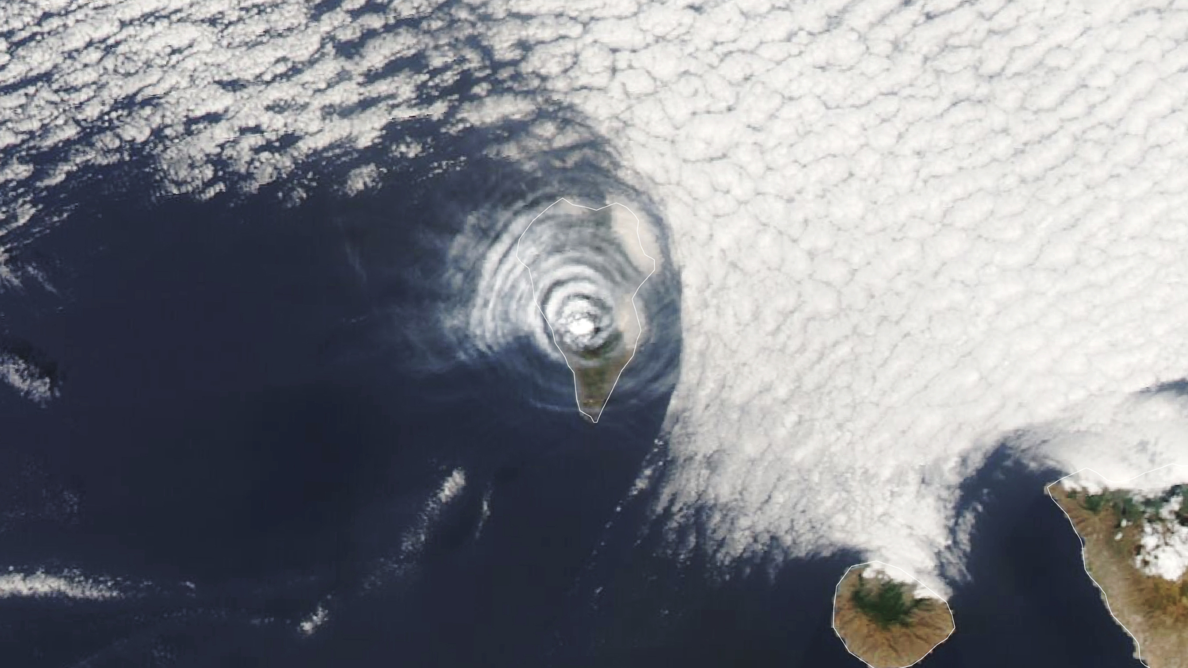 Une photo satellite d’une île couverte d’anneaux nuageux concentriques au milieu de l’océan