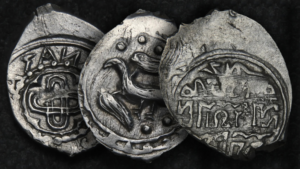 three stamped silver coins slightly overlapping one another against a black background